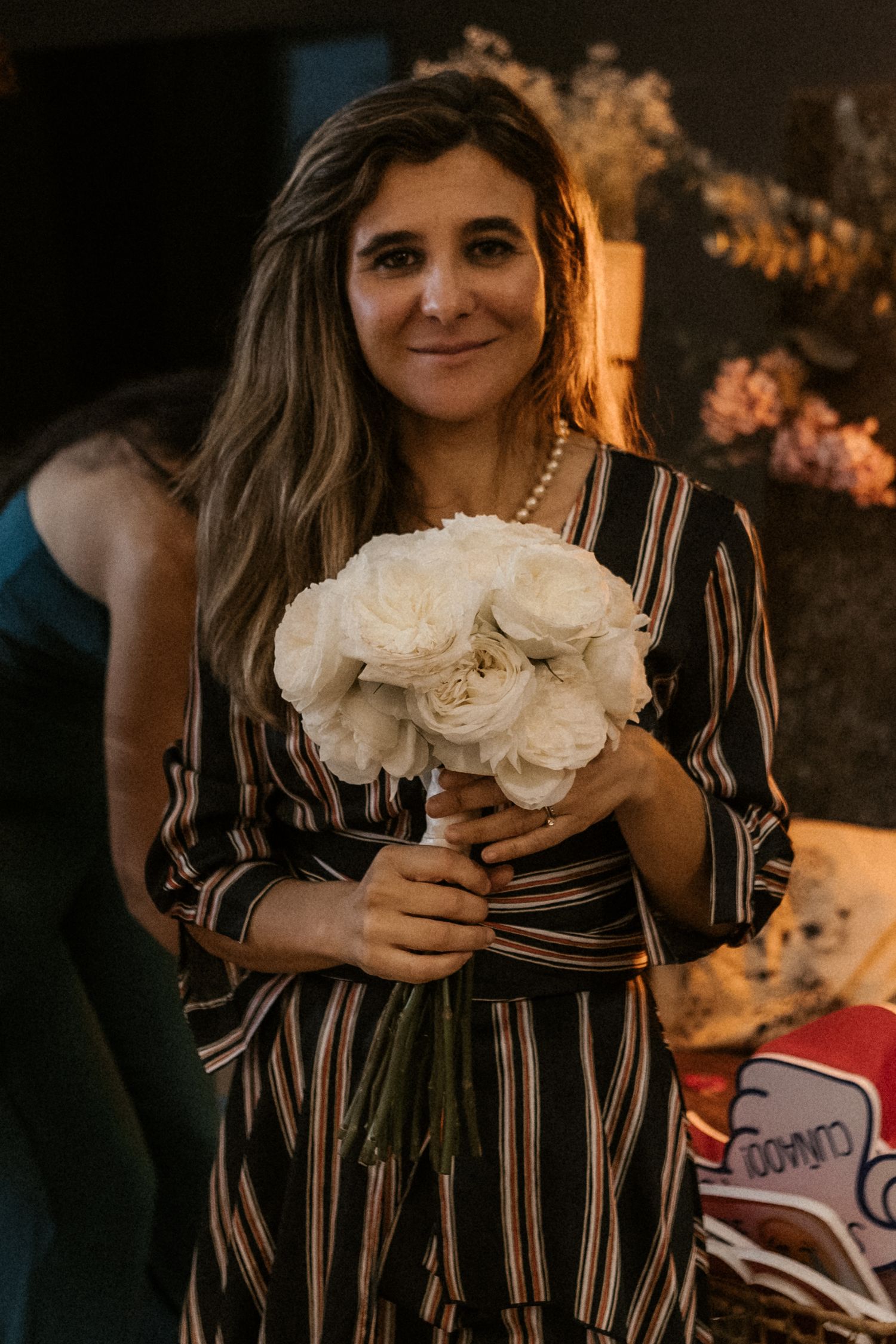 A guest in a striped dress holds a beautiful bouquet of white roses at an evening event.