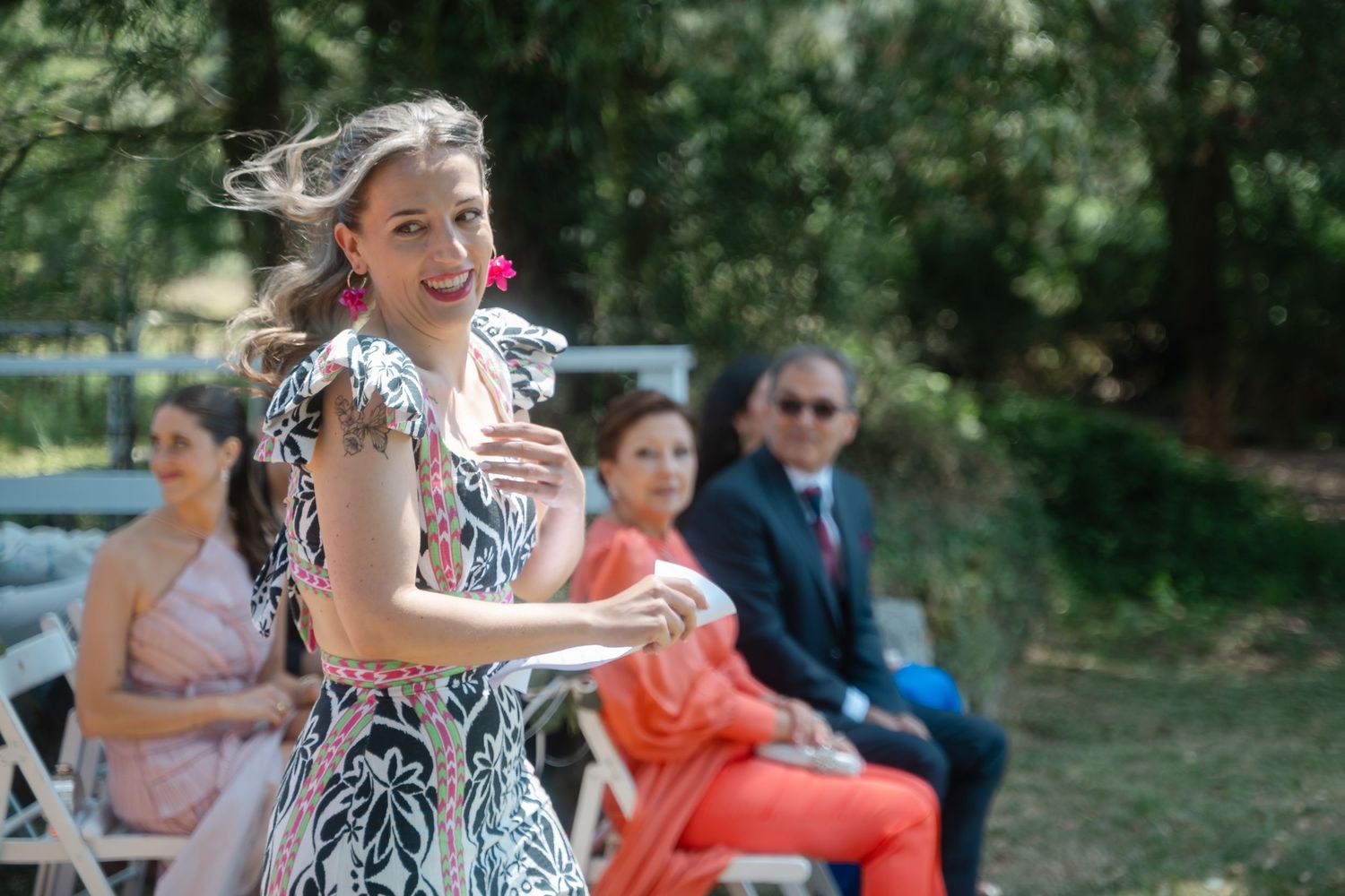 Wedding guests seated outdoors in a garden setting with natural greenery in the background.