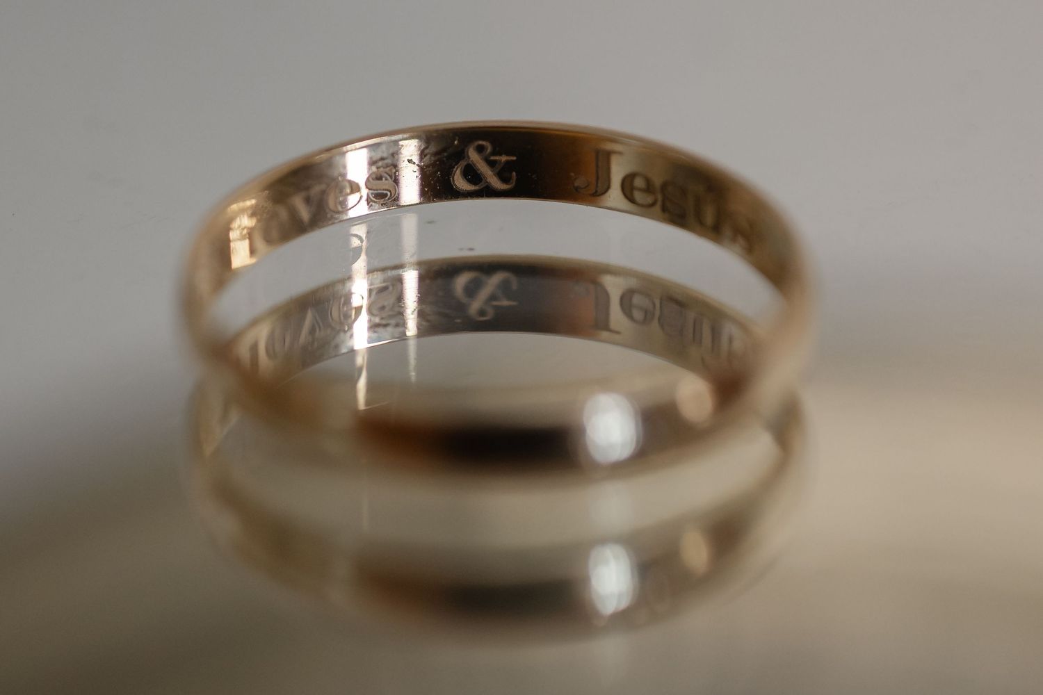 Close-up macro shot of two gold wedding bands with engraved text reflecting on a light surface.