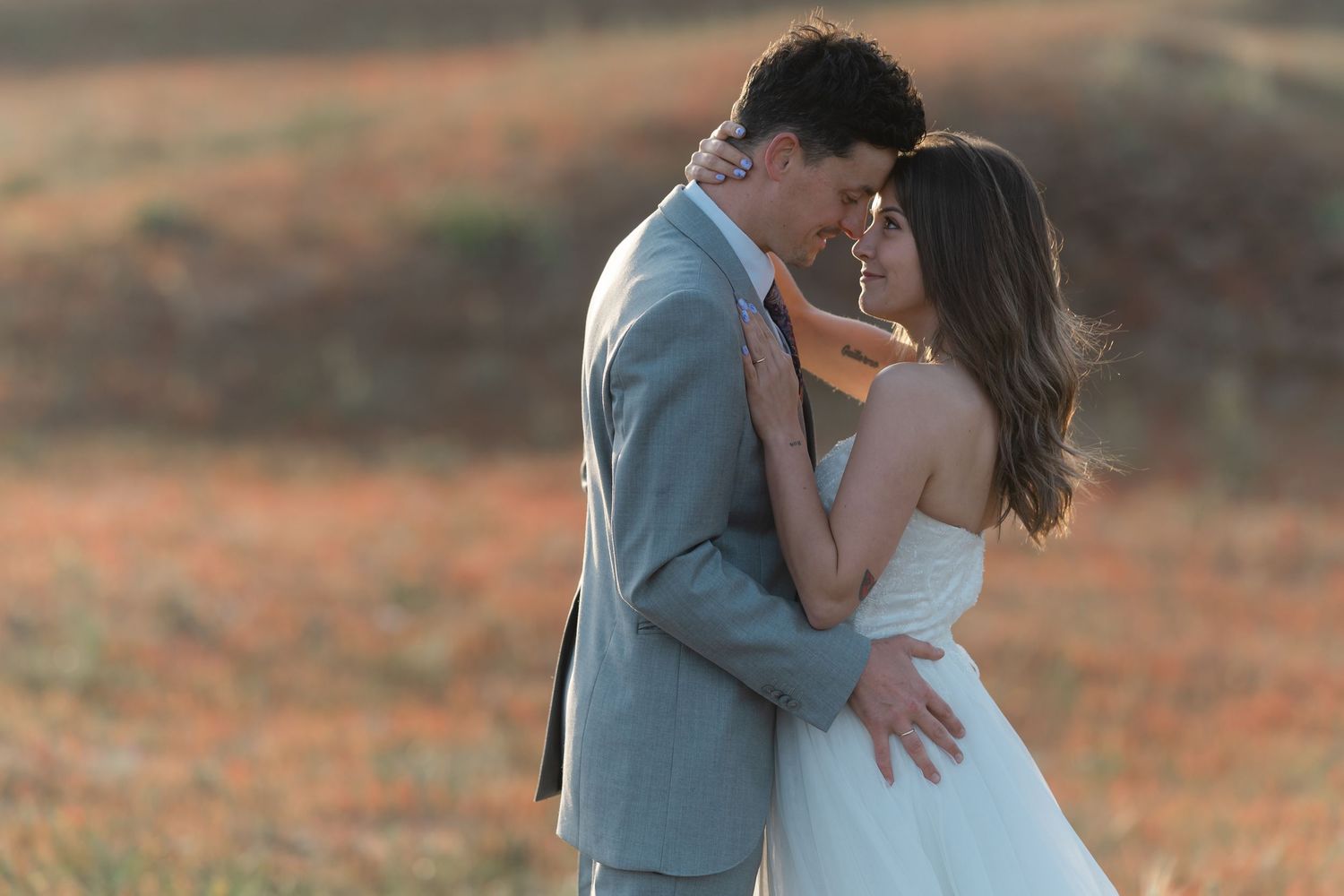 Bride and groom touch foreheads tenderly in a colorful field during golden hour wedding shoot.