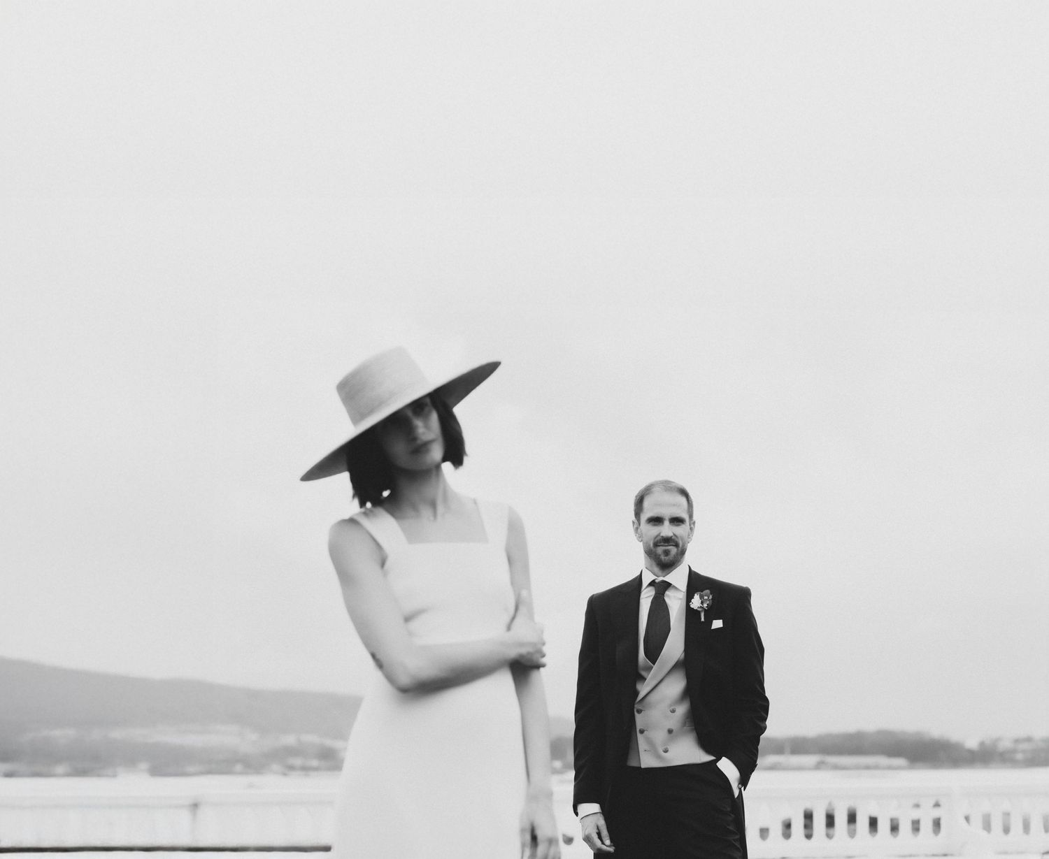 A vintage black and white wedding photo showing a couple outdoors with a scenic backdrop.