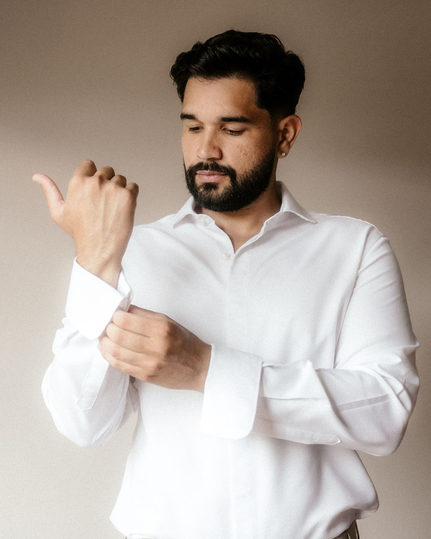 A person in a white dress shirt adjusts their sleeve cuff against a neutral beige background.