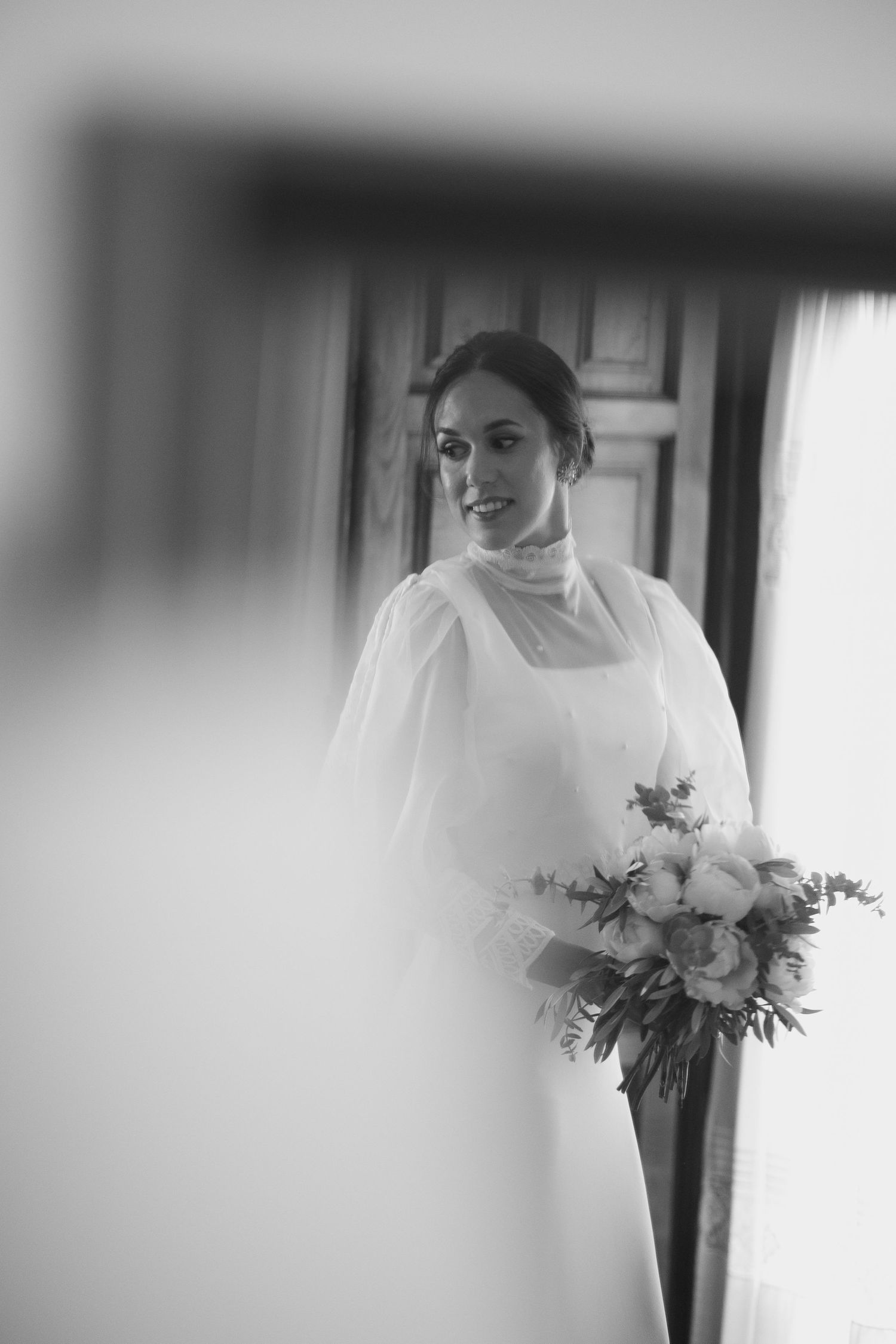 Ethereal black and white sequence of a bride in a flowing dress holding a floral bouquet near a window.
