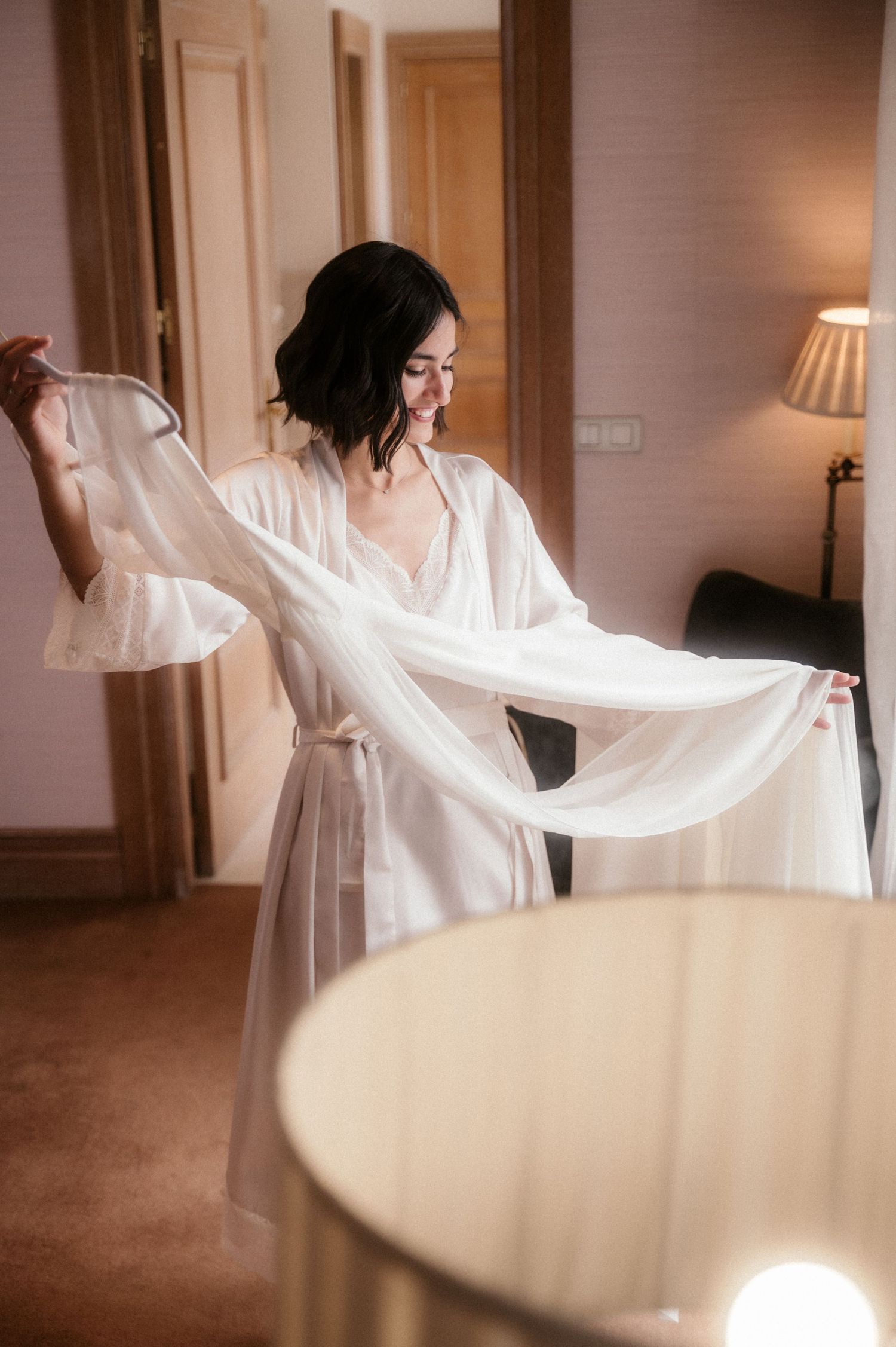 A person in white twirls gracefully with flowing fabric in a warm-lit room creating an ethereal dance-like movement series.