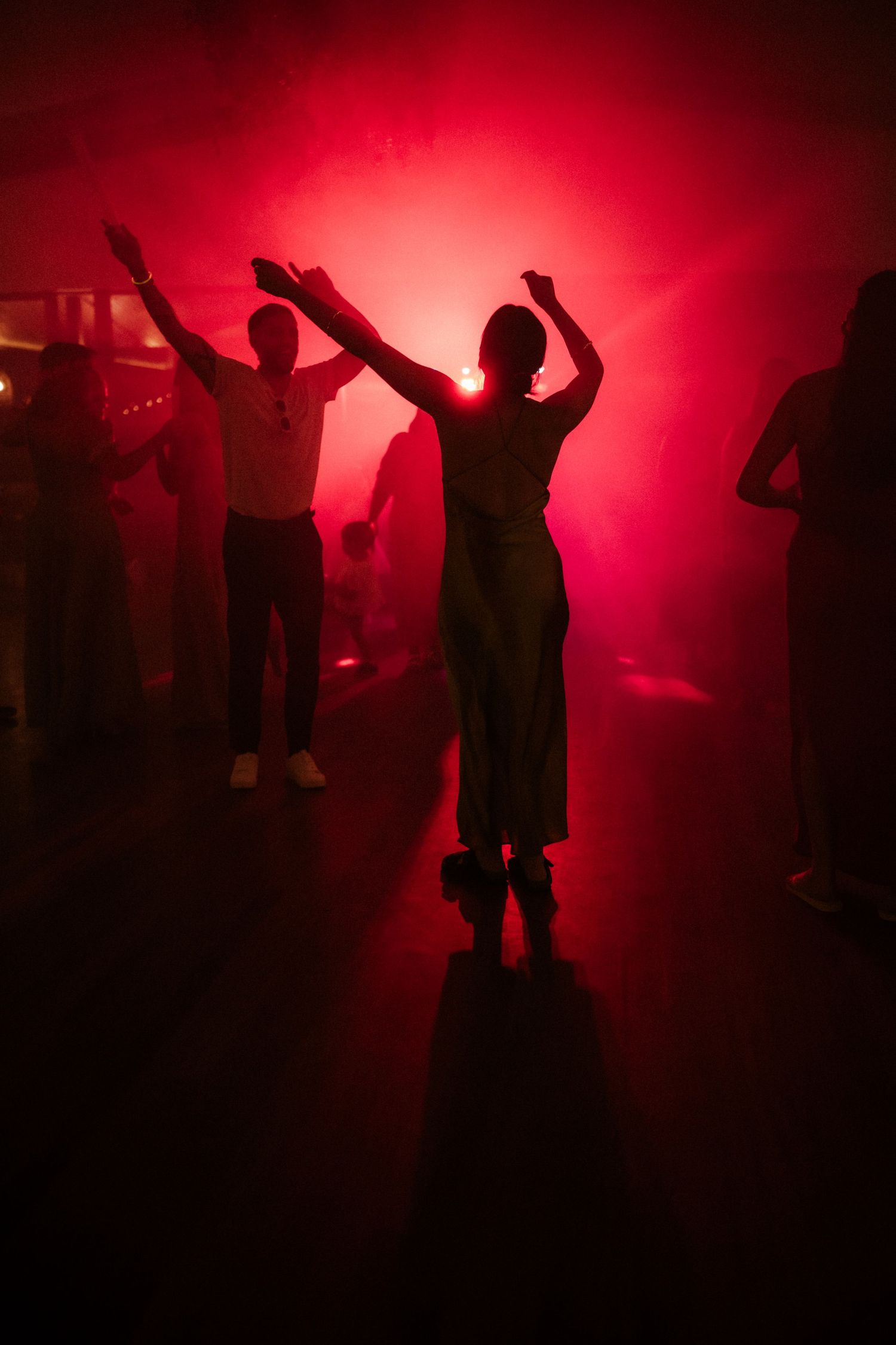 Silhouettes of people dancing in a dark nightclub with dramatic red lighting and smoke effects creating an atmospheric mood.
