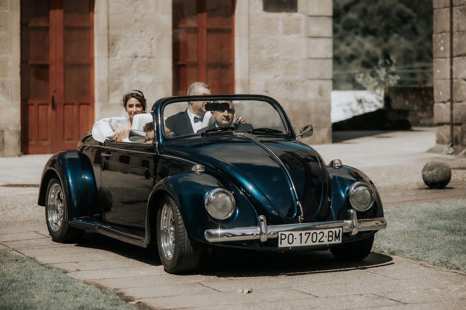 A collection of vintage black luxury cars parked in a row along a stone building exterior.