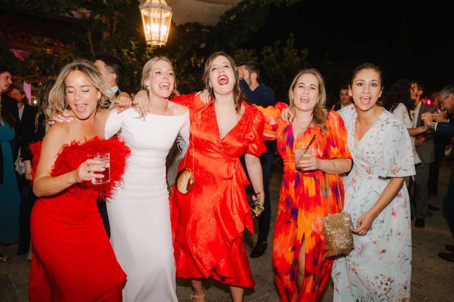 Wedding guests in vibrant red and orange dresses celebrate on the dance floor during the reception.