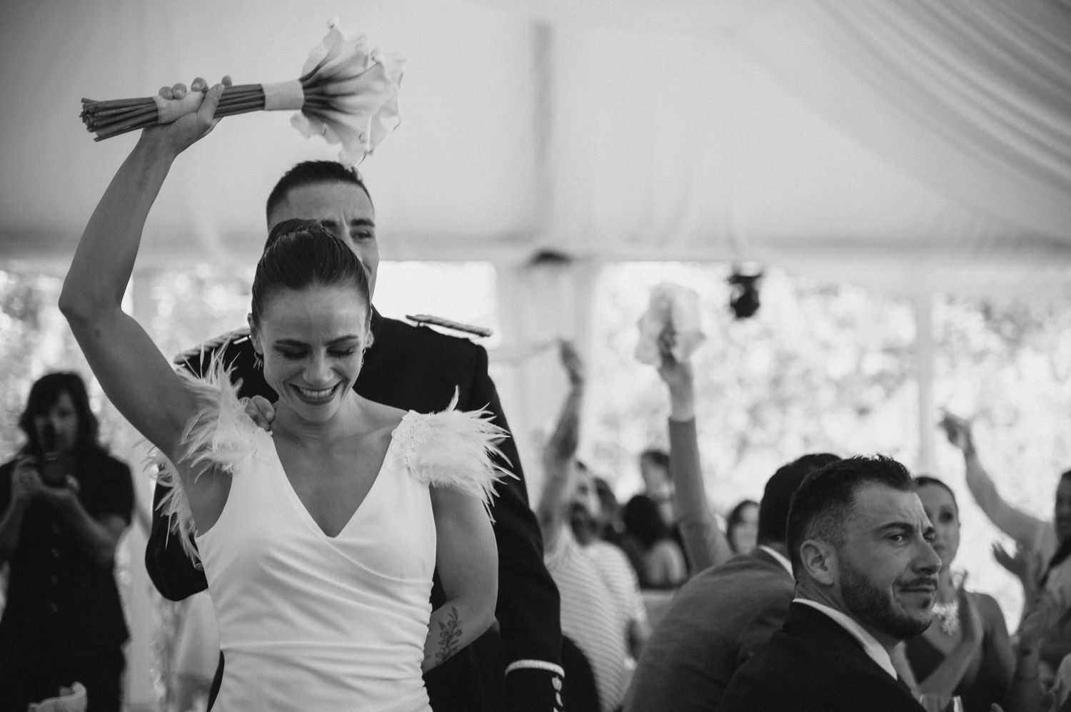 Black and white photo of wedding guests dancing and celebrating at a tented reception.