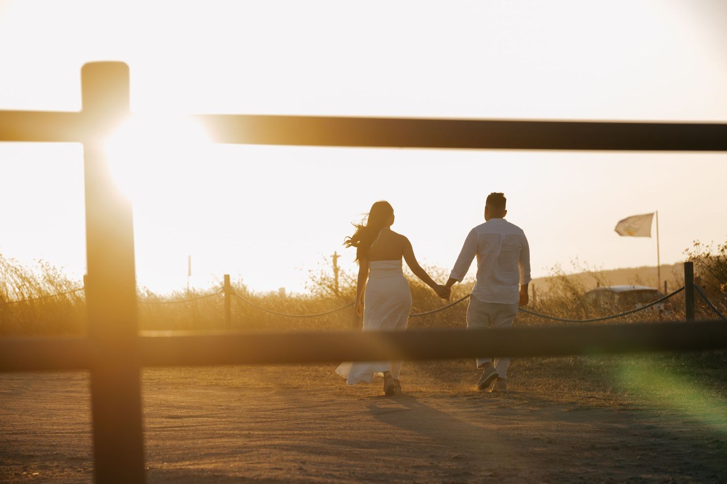 Silhouettes of people against a golden sunset sky with a fence in the background.