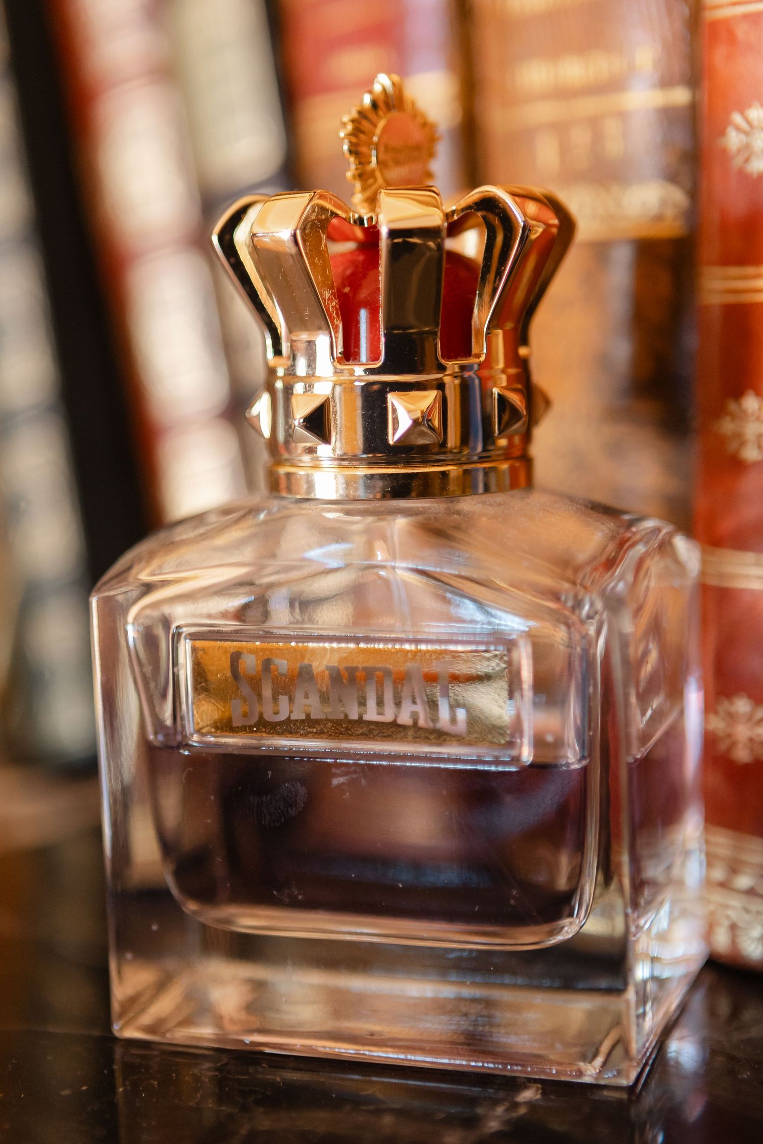 Glass perfume bottles with gold crown-shaped caps sit in a row against a blurred background of books.