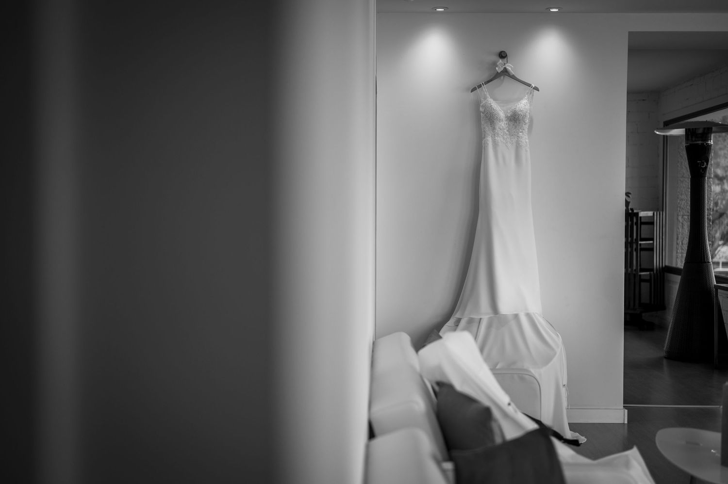 A wedding dress hangs elegantly in a brightly lit room with recessed lighting and white walls.
