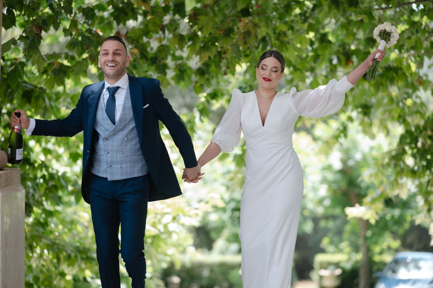 A couple shares a joyful dance moment outdoors surrounded by green trees and natural lighting.