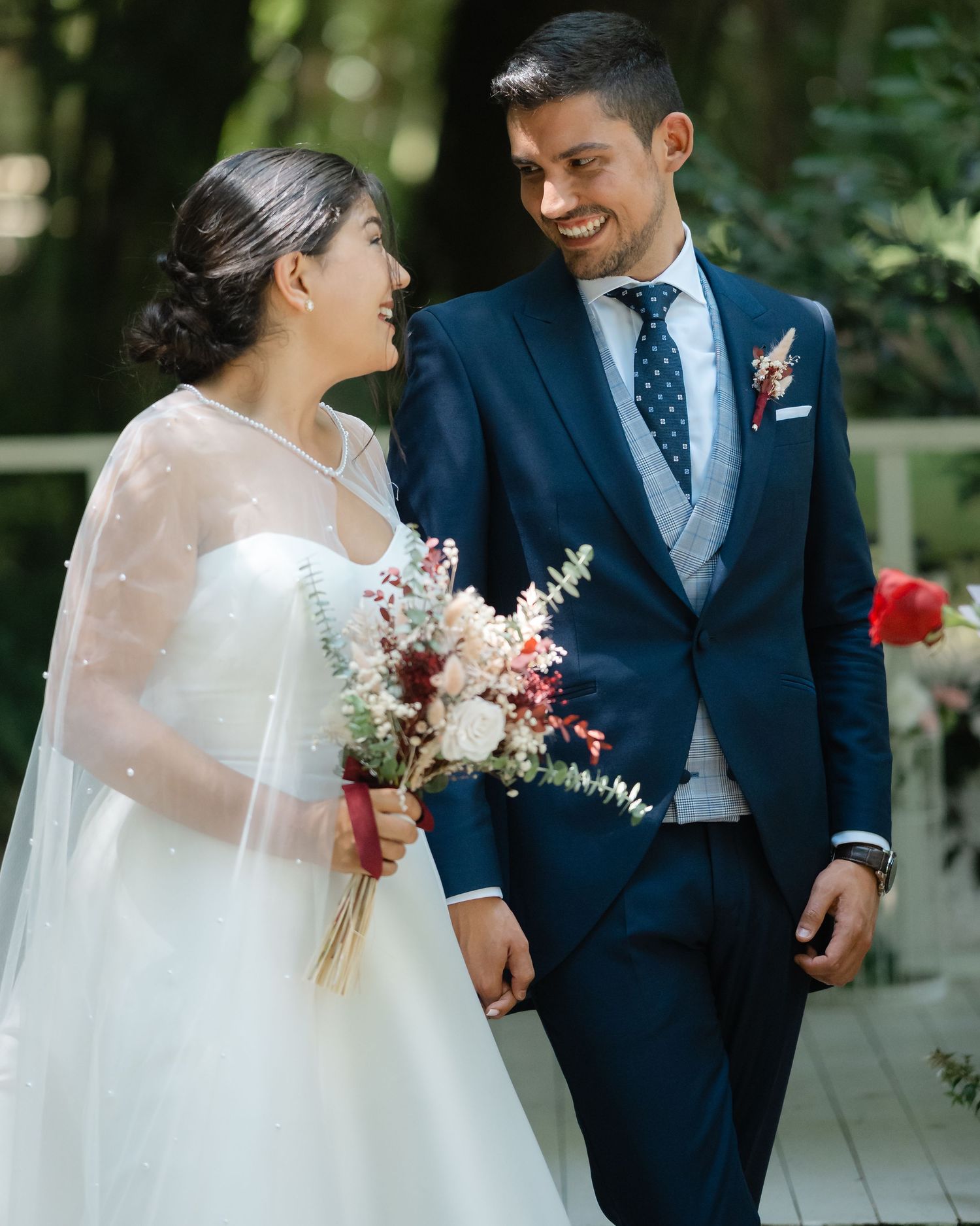 A couple shares a joyful moment in an outdoor wedding setting with the bride in white and groom in navy suit.