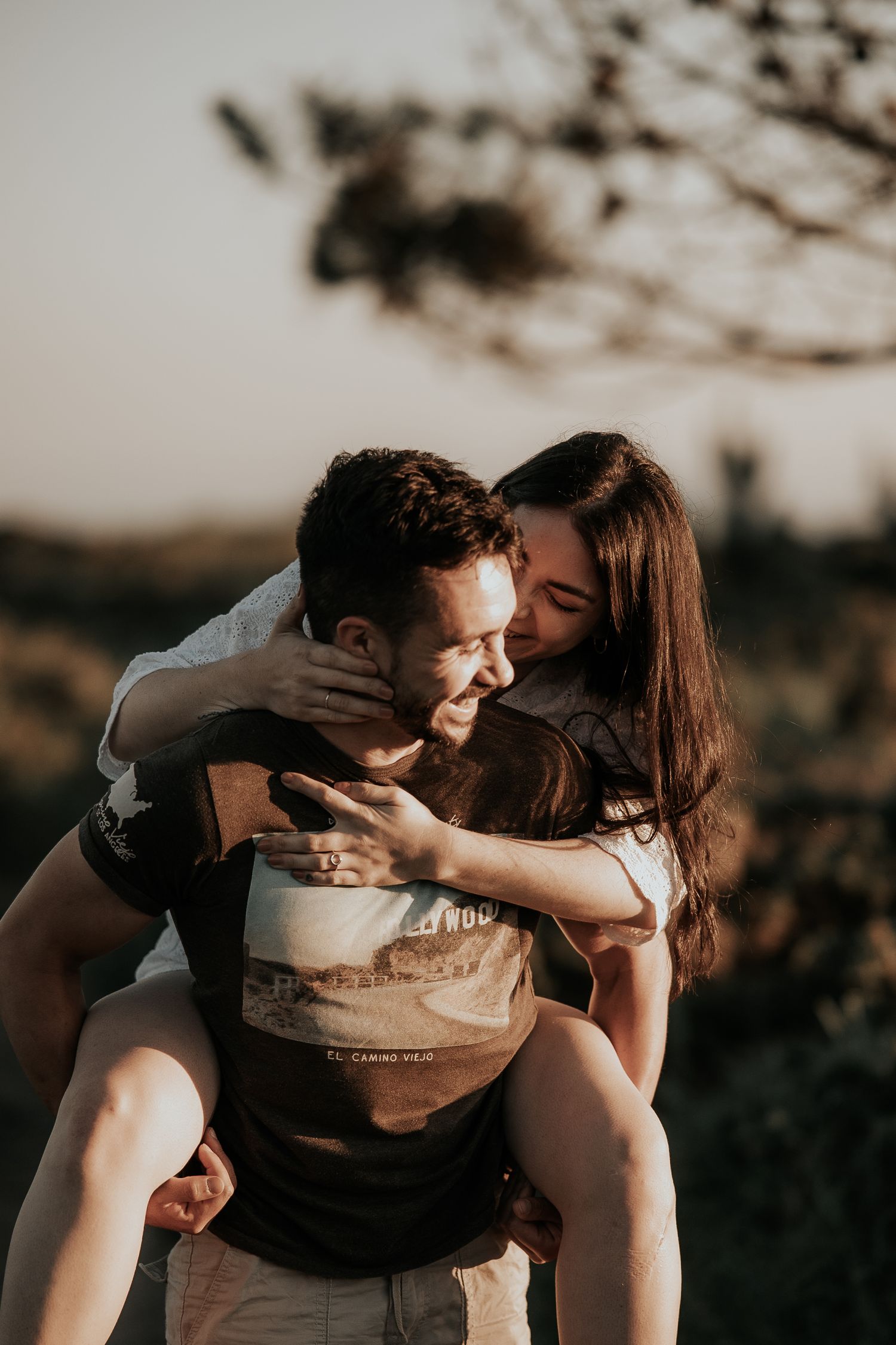 A romantic couple shares an intimate embrace and kiss in a moody outdoor setting at sunset.