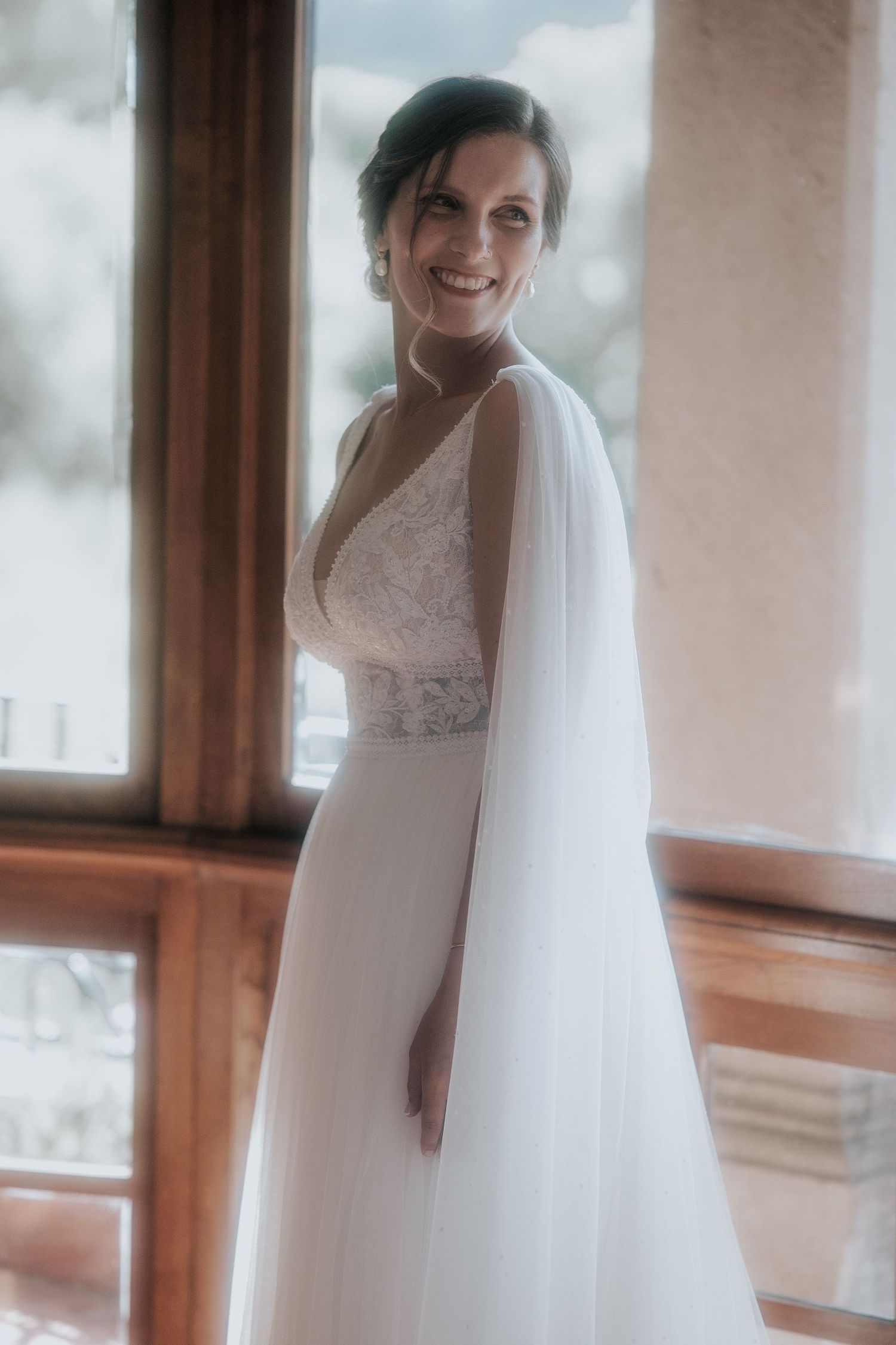 A bride in a white lace wedding dress and flowing veil poses gracefully by a window in a series of candid moments.