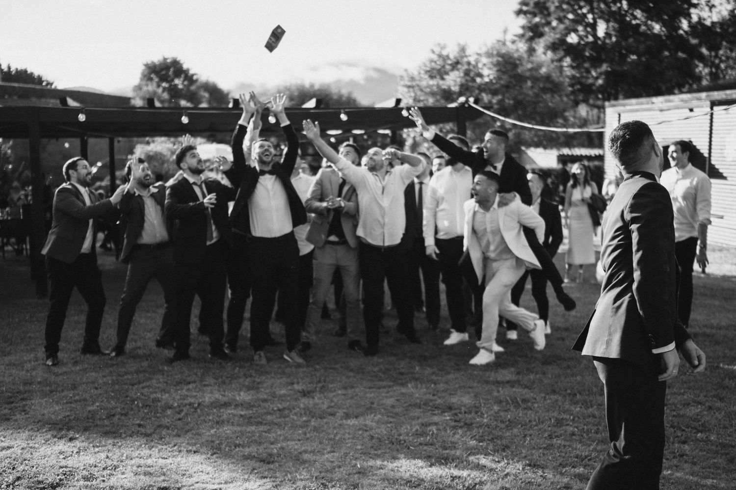 A group of people in formal attire dancing in a line outdoors during what appears to be a wedding celebration.