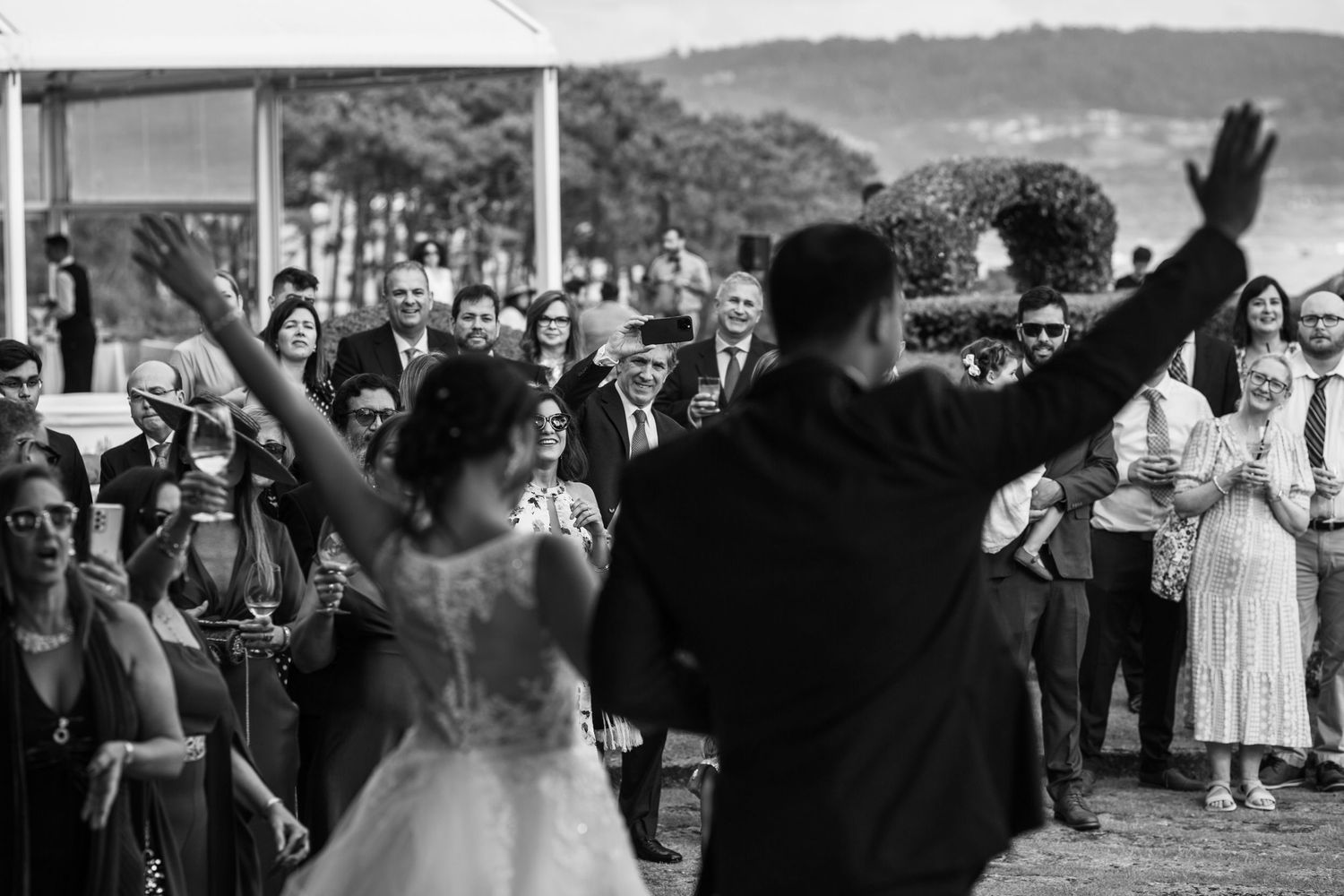 Wedding celebration with guests cheering and waving as couple dances outdoors.