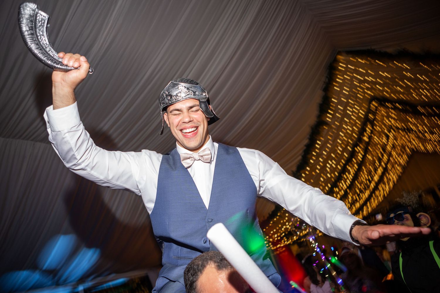 Wedding party dancing energetically under dramatic lighting at an indoor reception venue.