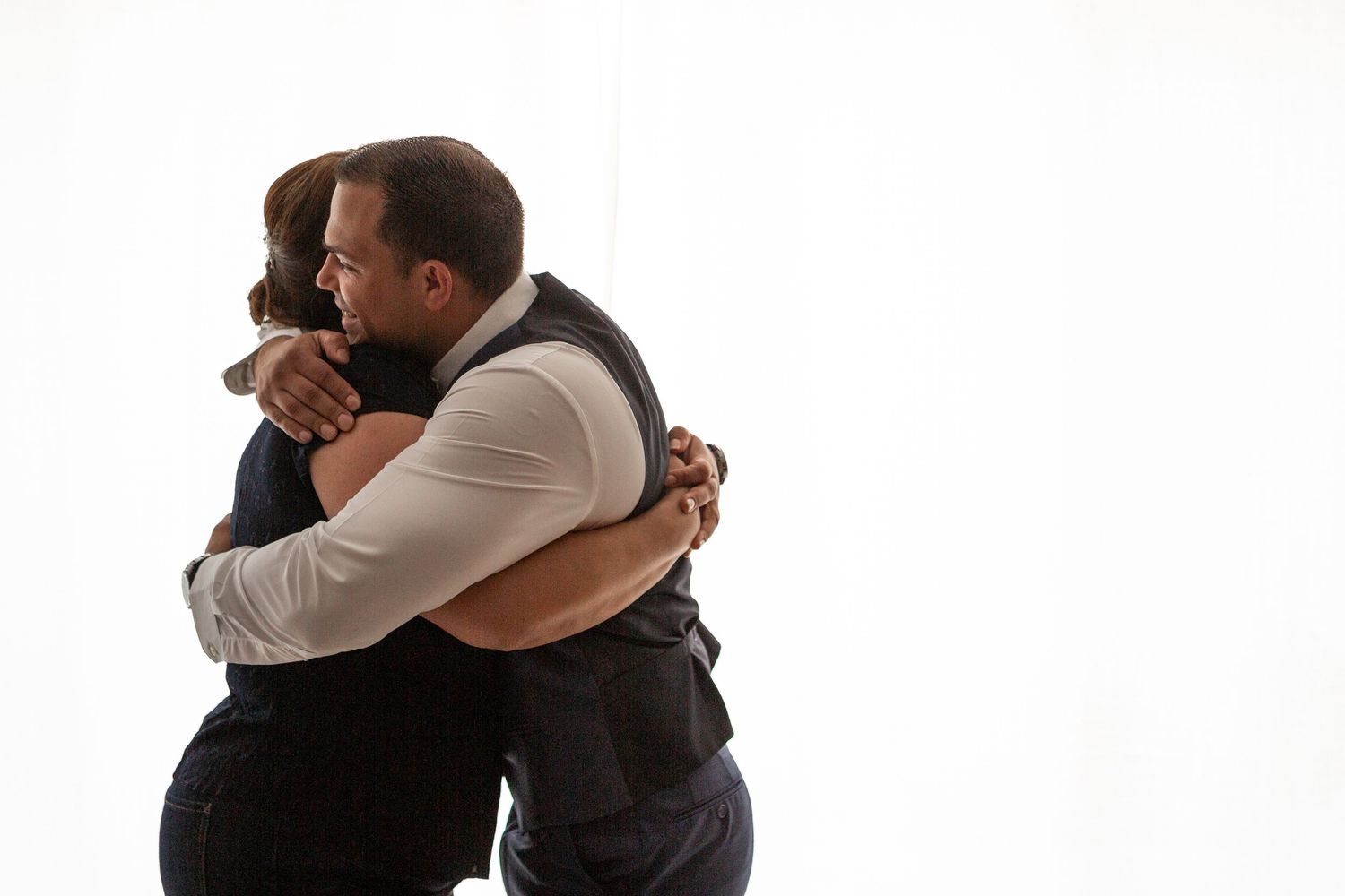 Two people embrace in an emotional hug against a white background.