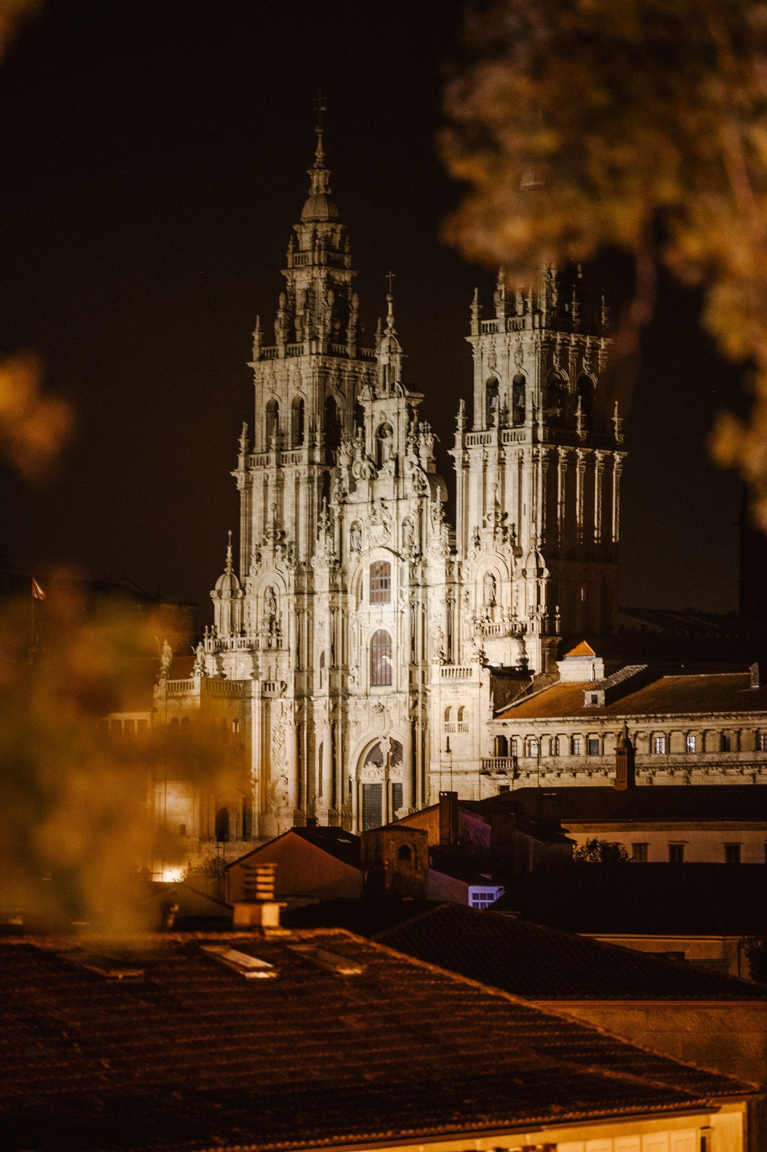 Gothic cathedral spires illuminated at night against a warm amber sky with rooftops in the foreground.