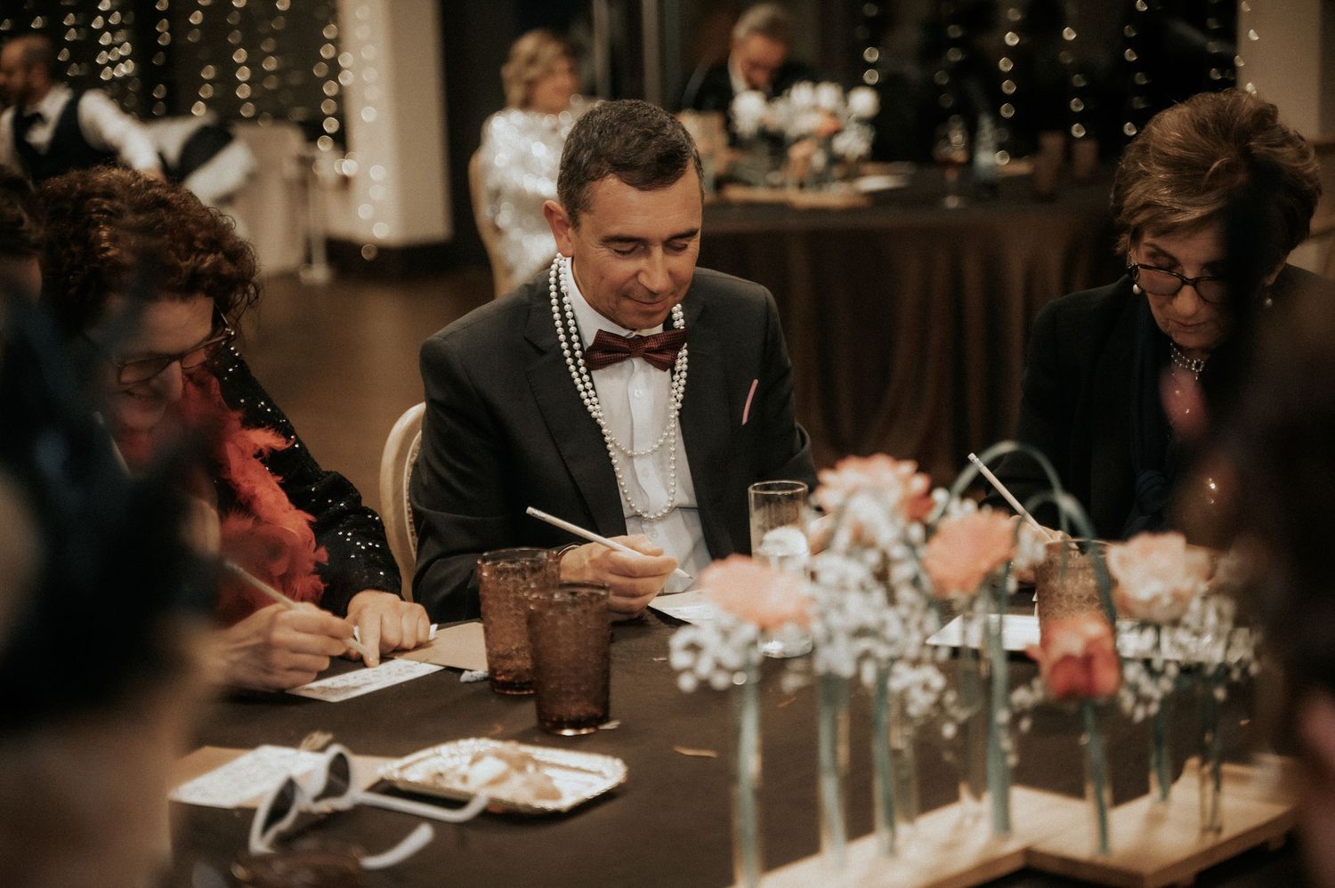 People gathered at an elegant dinner party with bow ties and formal attire seated around a table with decorative centerpieces.