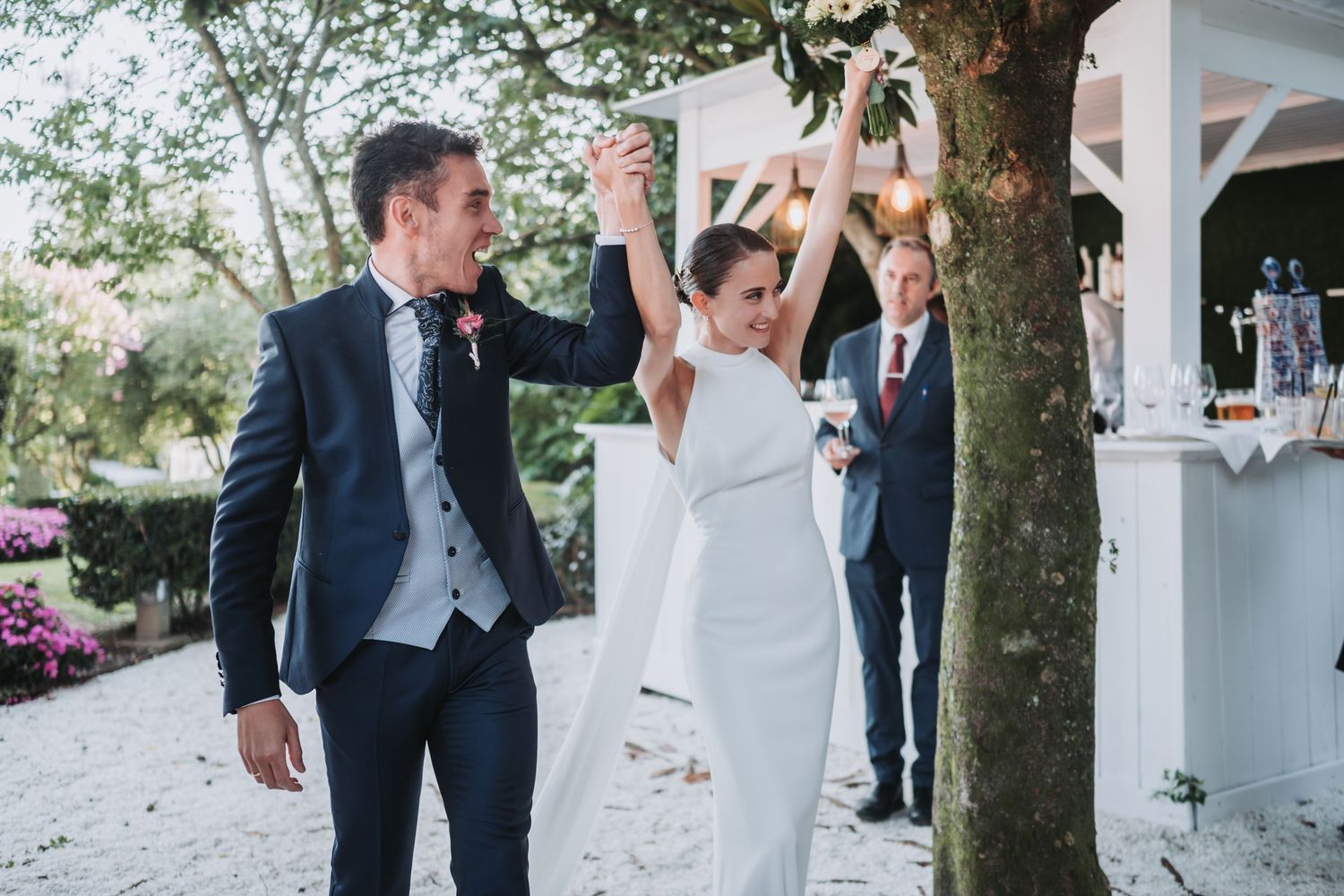 A joyful wedding celebration with guests dancing and laughing together in an outdoor garden setting.