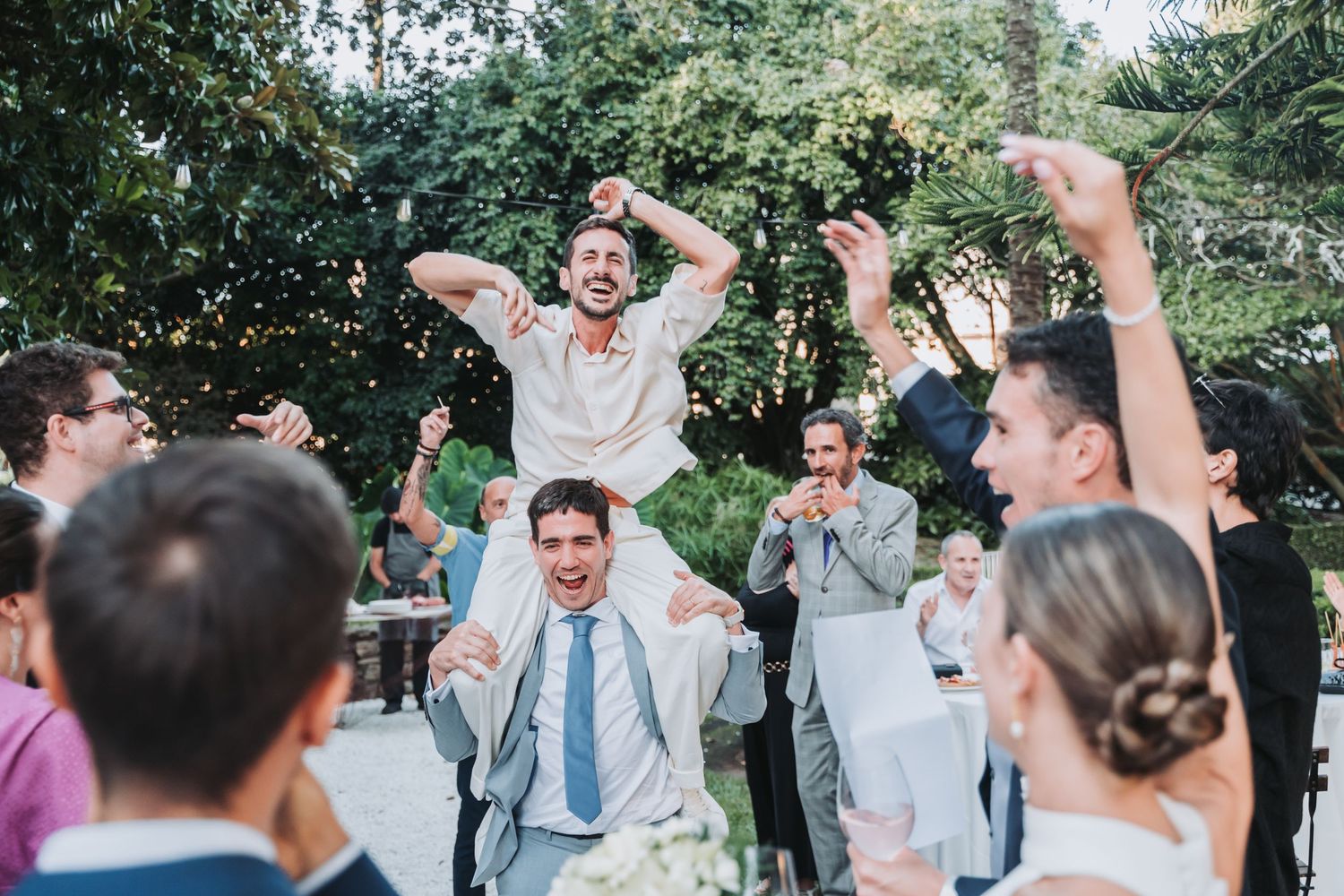 Wedding party celebrates outdoors with raised hands and joyful expressions.