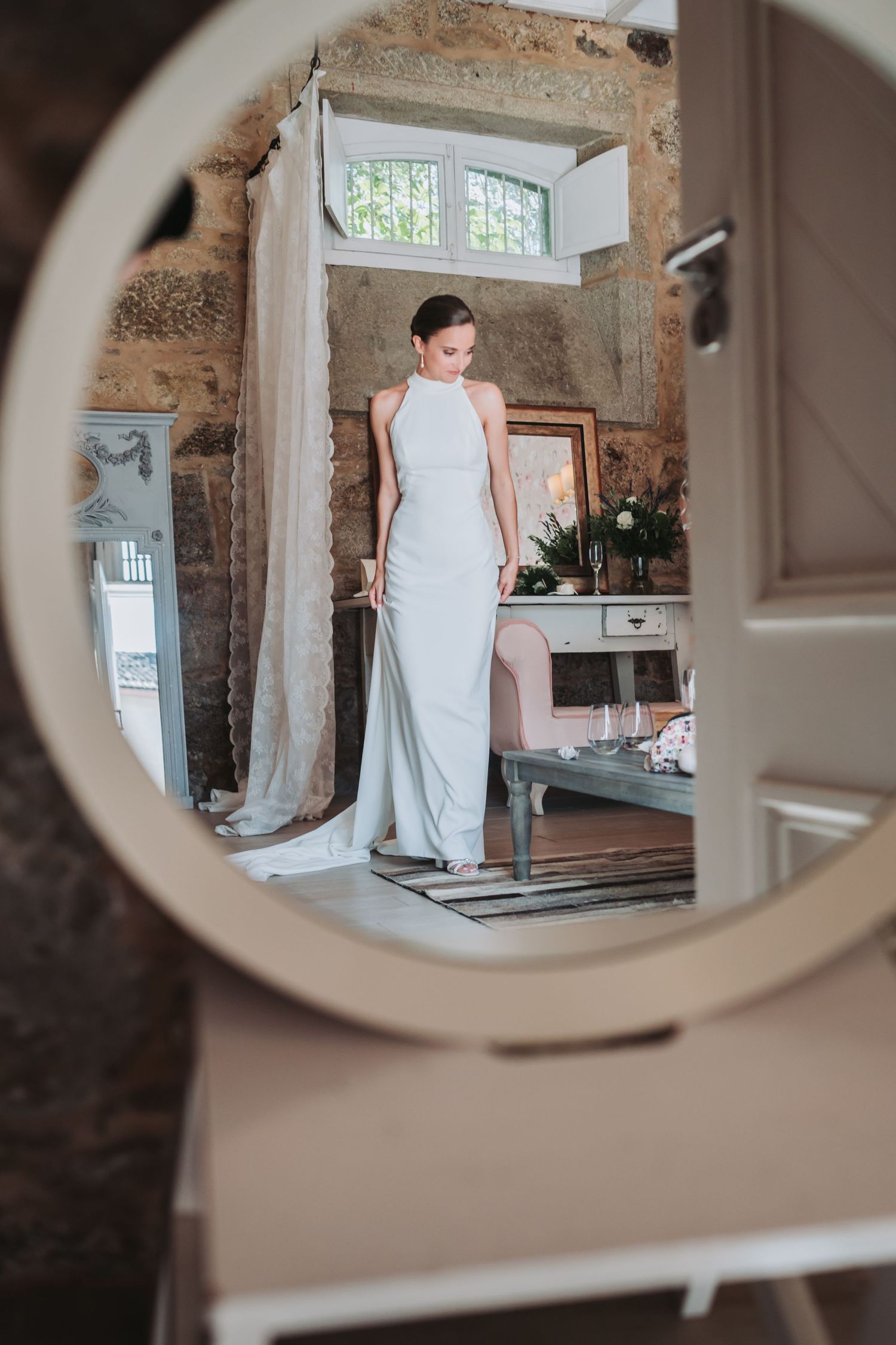 Mirror reflection of white wedding dress in rustic room with stone walls.