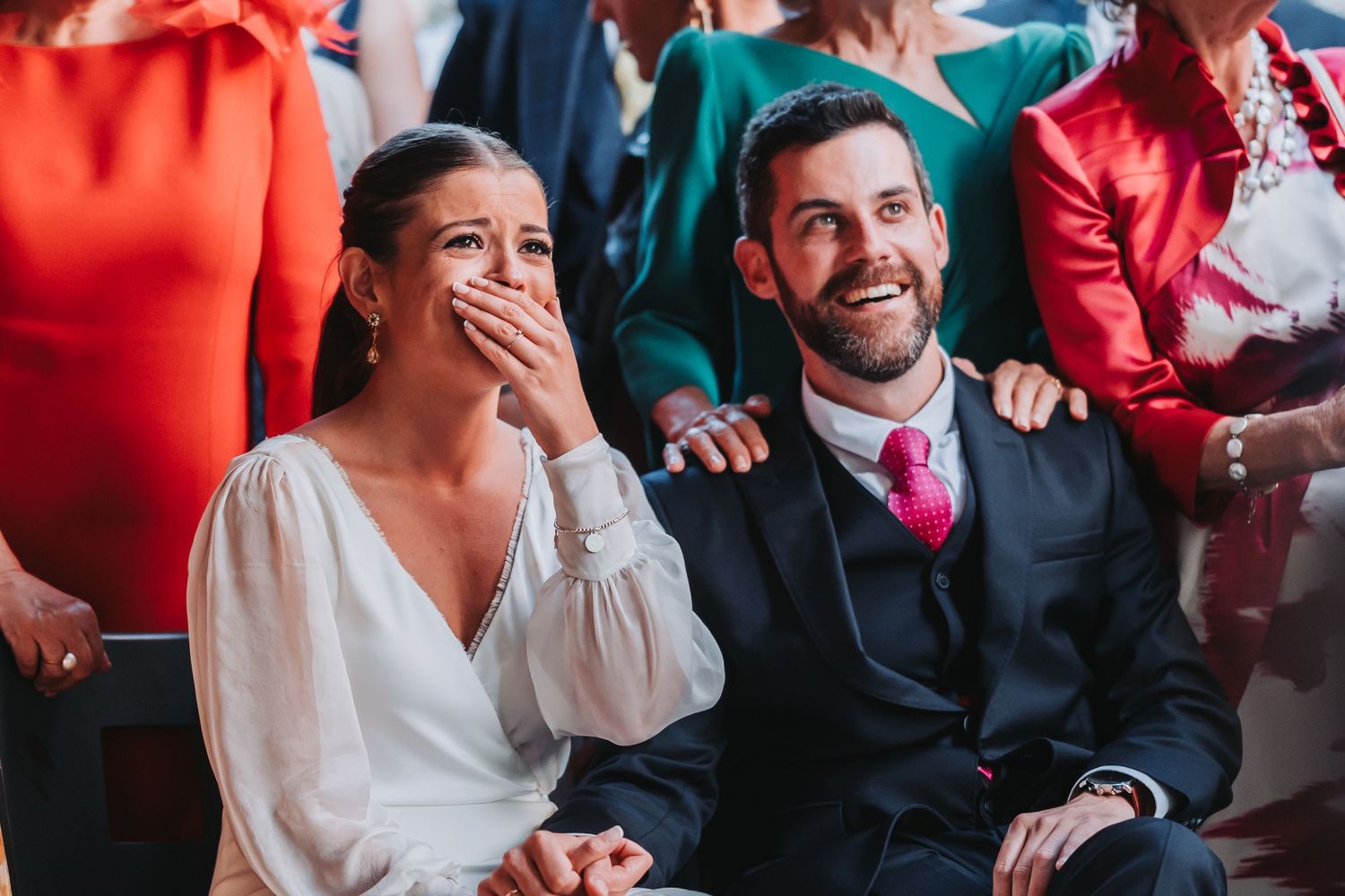 Wedding guests laugh and react emotionally during a reception celebration at an indoor venue.