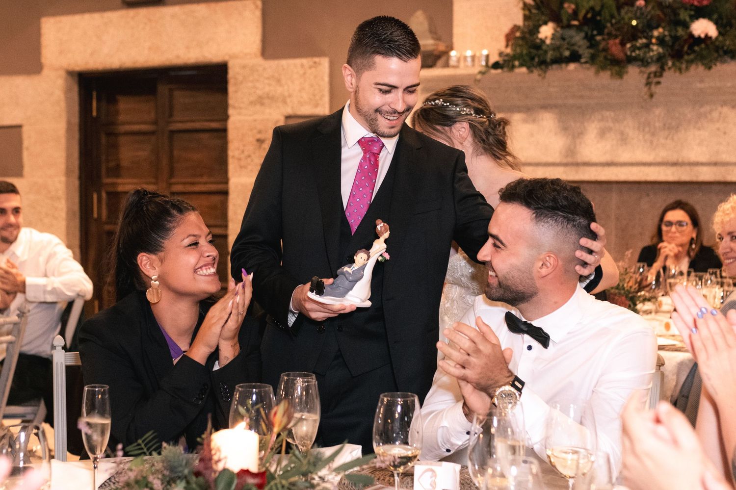 Wedding guests seated at an elegant reception dinner table with candlelight and floral centerpieces.