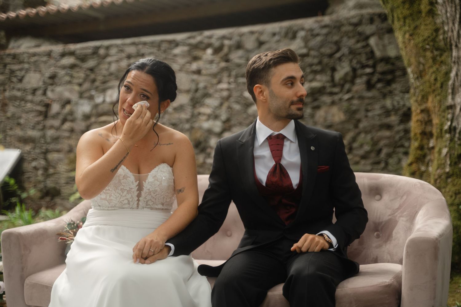 Couple shares candid moments on a beige couch during their outdoor wedding.