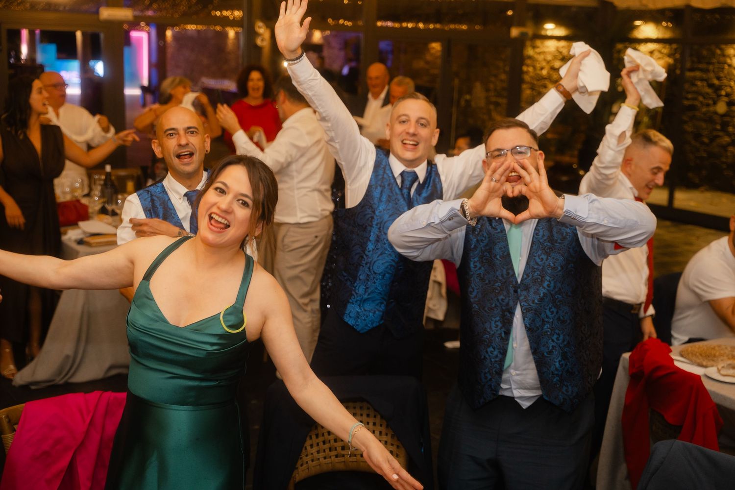 Guests at a wedding reception react with excitement and laughter during a celebratory moment.