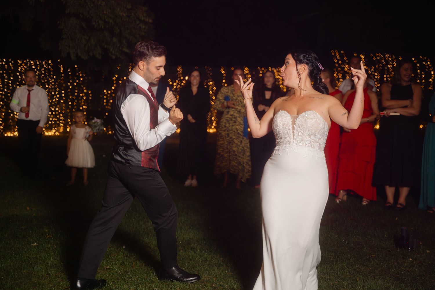 Couples dance together at an evening wedding reception with twinkling lights in the background.