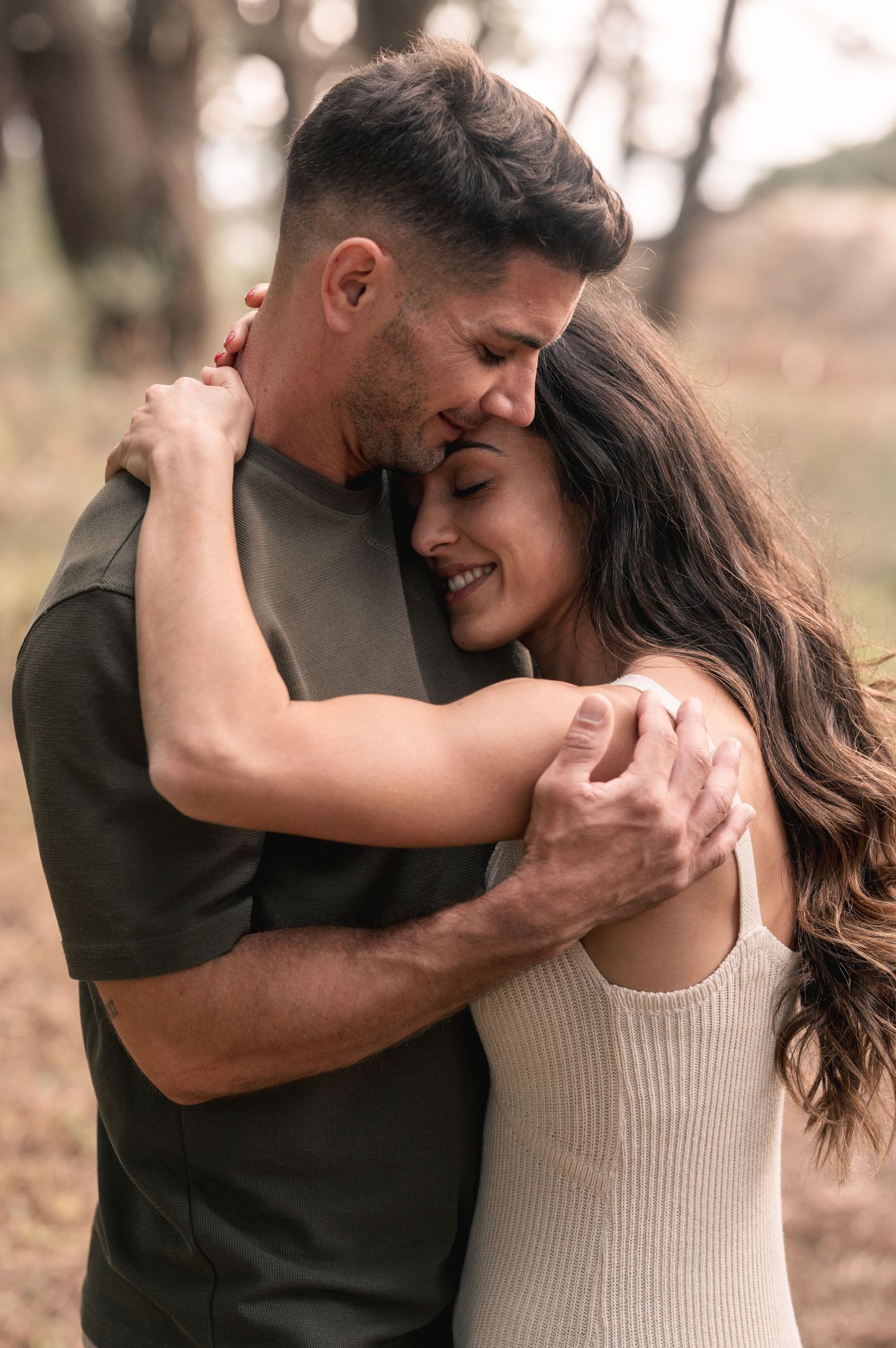 Romantic couple embraces and dances together in a natural outdoor setting with soft bokeh lighting.
