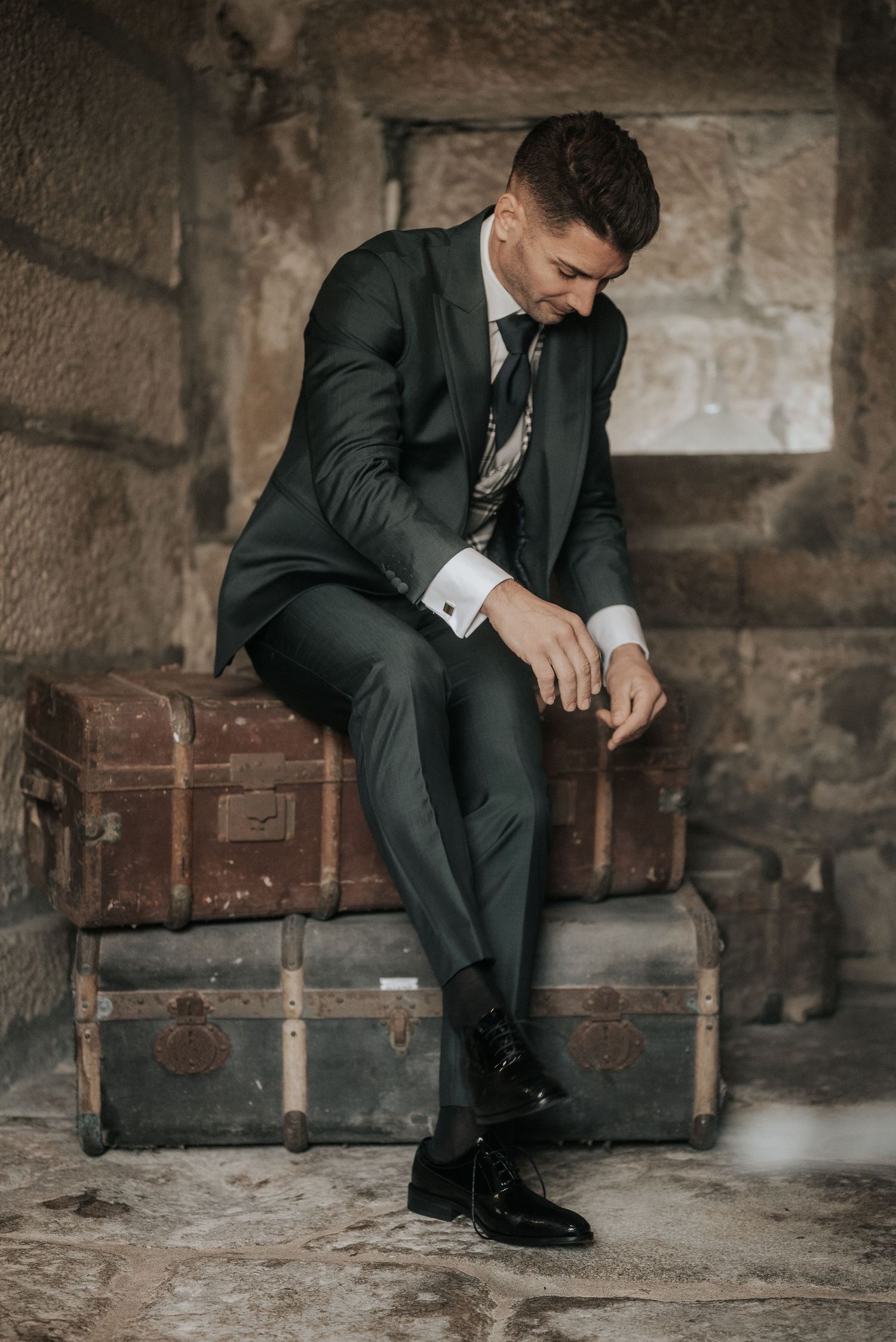 A person in a dark suit sits contemplatively on wooden steps in an industrial setting.