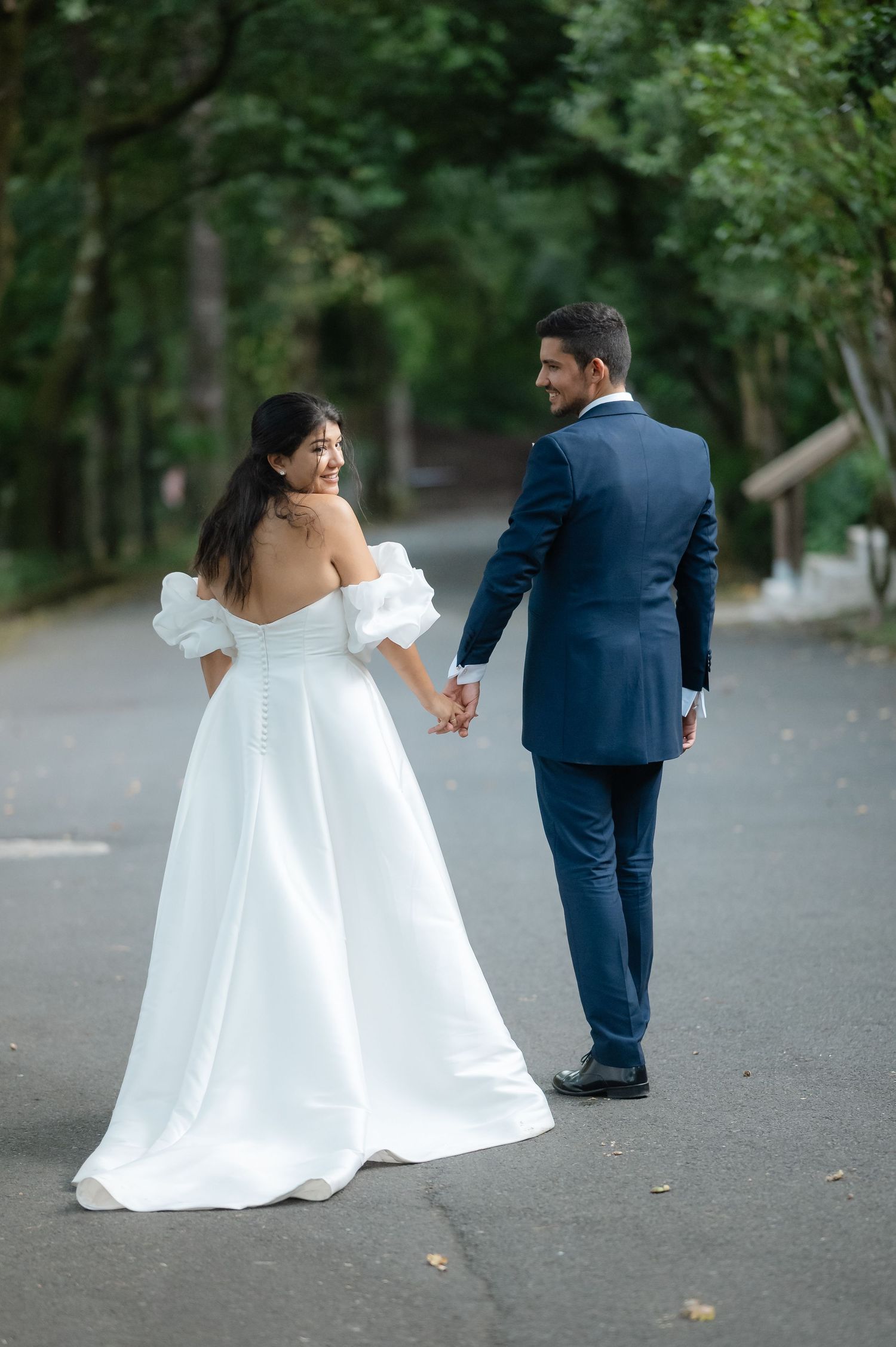 Wedding couple in navy and white dancing and twirling on a tree-lined pathway.