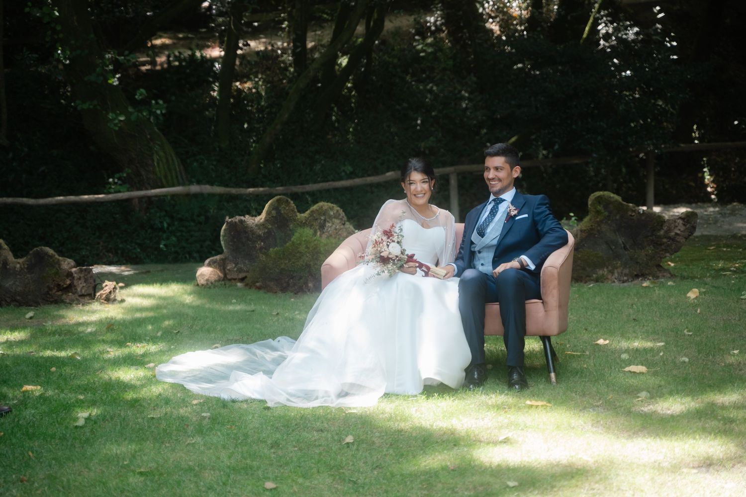 A couple relaxes together on a blanket in a sunlit garden setting during a wedding photo session.