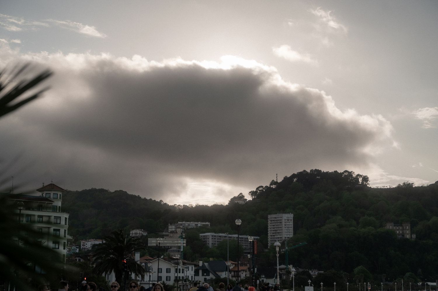 A dramatic panoramic view of dark storm clouds gathering over coastal mountains and buildings at dusk.