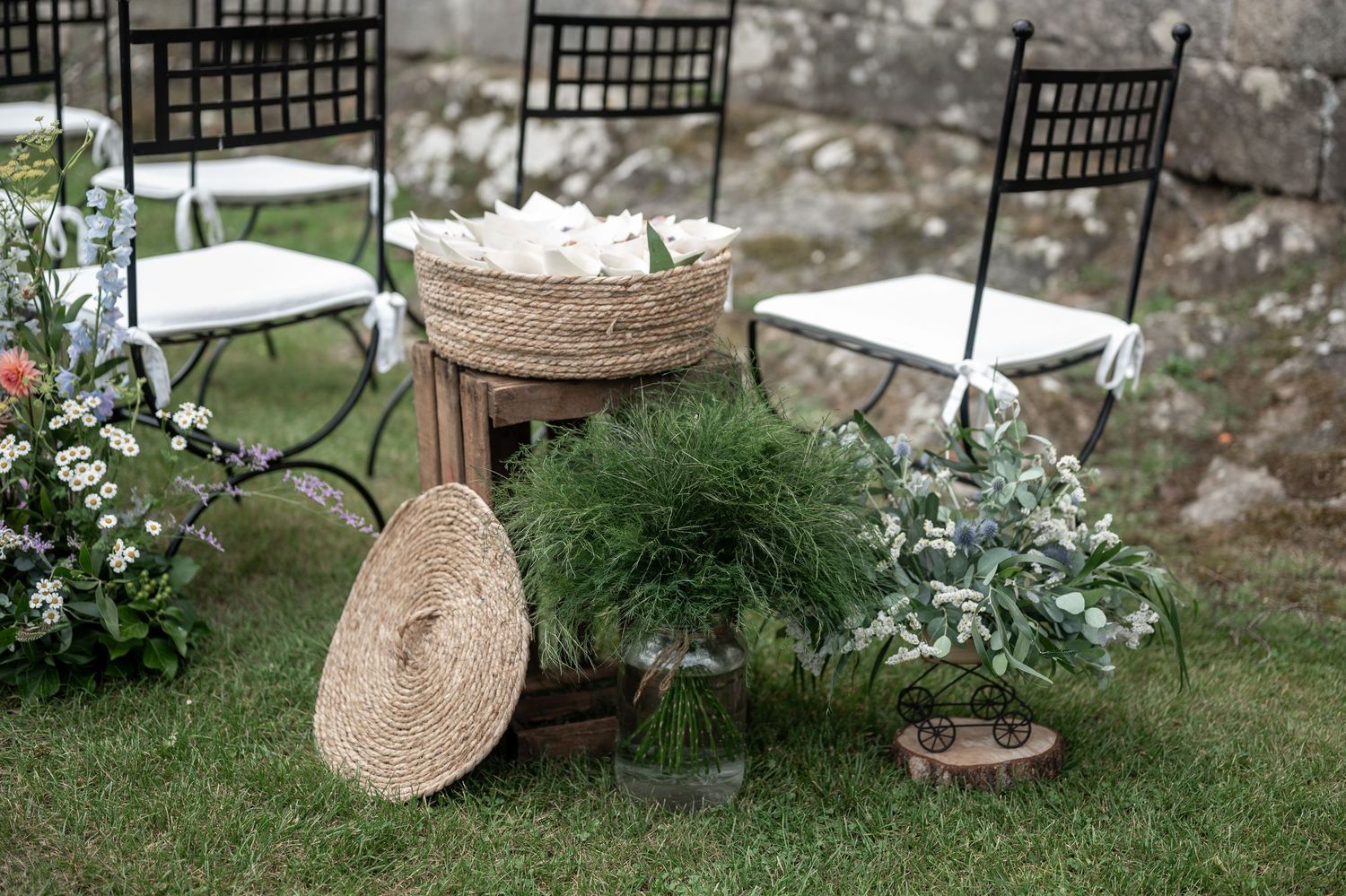 Black metal garden chairs and woven basket decor arranged on a grassy lawn for an outdoor event setup.