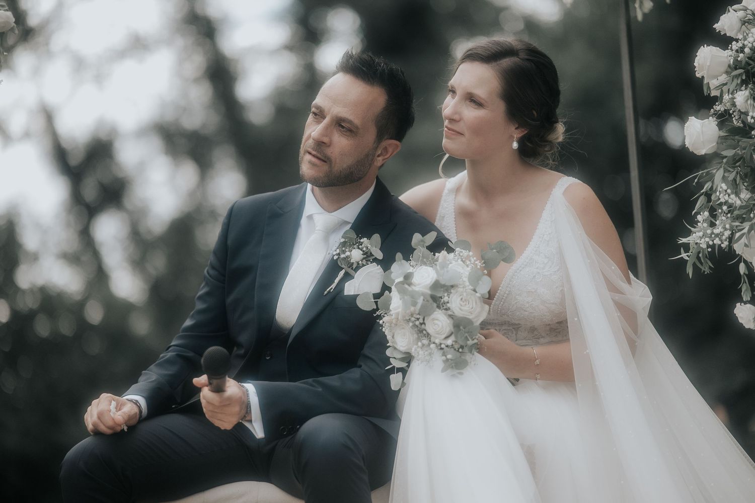 Newlyweds share tender moments during outdoor wedding ceremony surrounded by white flowers.