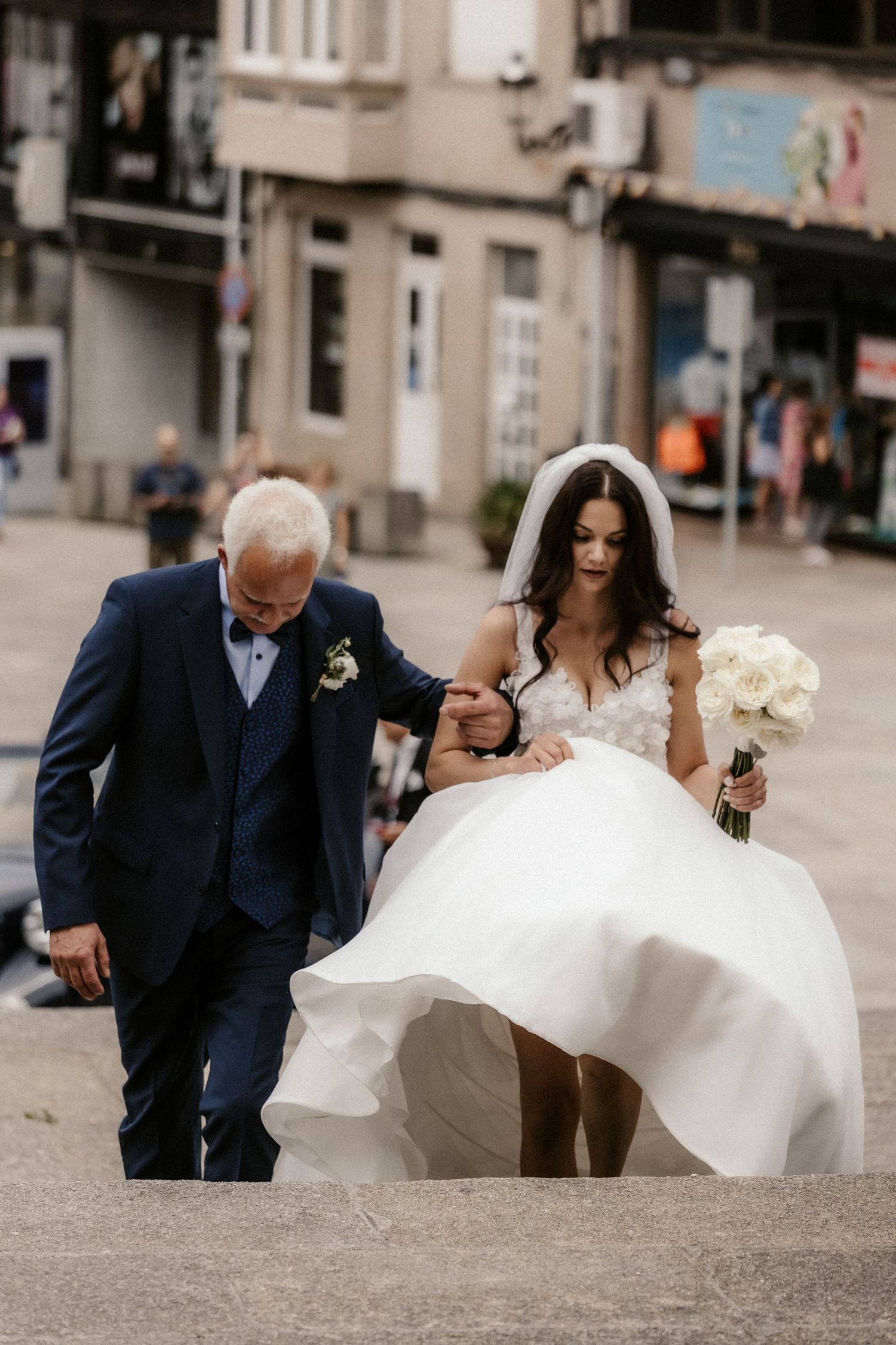 Wedding party walking on cobblestone street with flowing white wedding dress and navy suits.