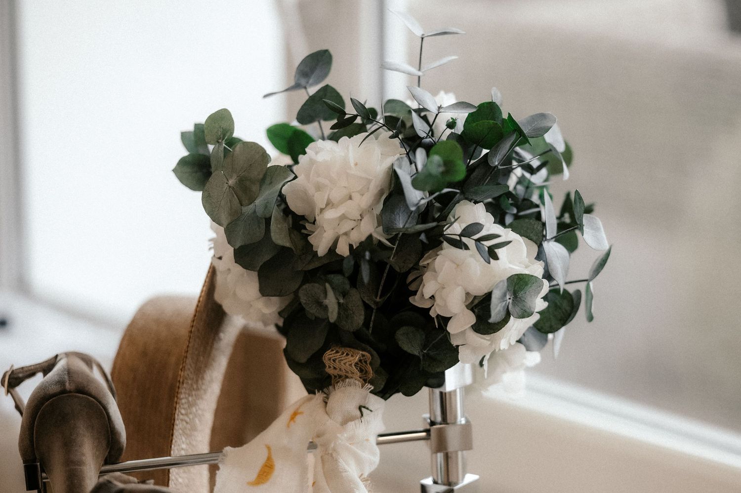 A rustic wedding table setting with white flowers in wooden vases and greenery garland against a light background.