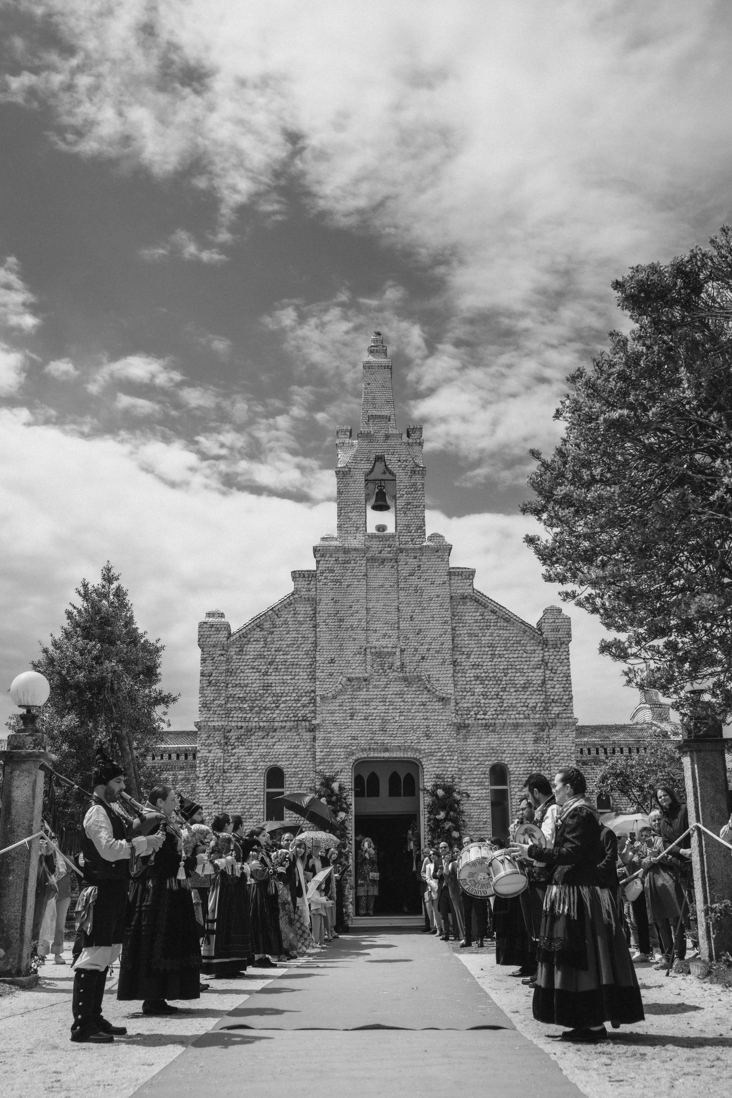 A traditional church wedding scene in black and white with guests in period dress forming a walkway outside a stone church.