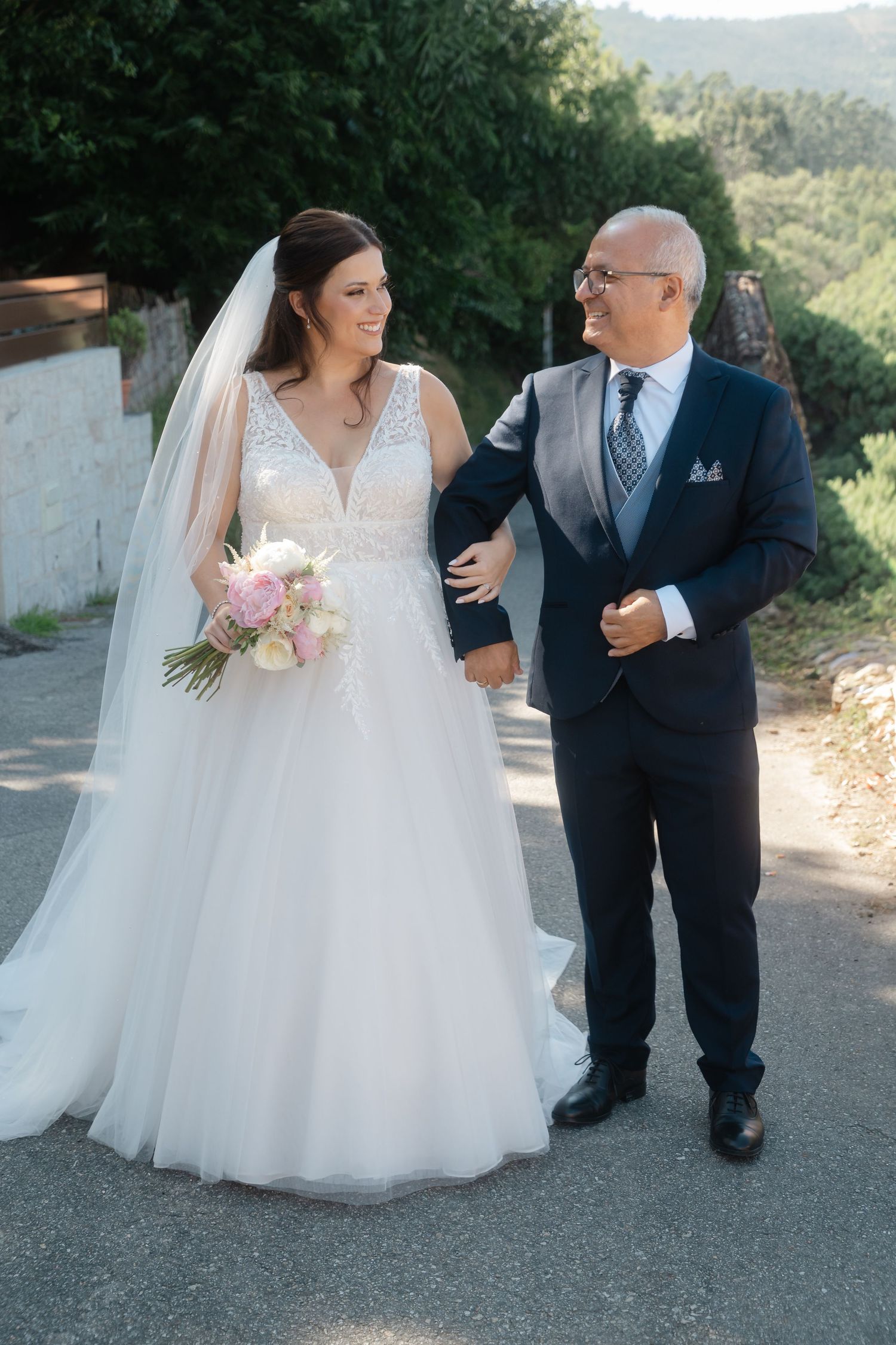 A beautiful outdoor wedding scene with a bride in a flowing white gown walking with a companion on a mountain path.