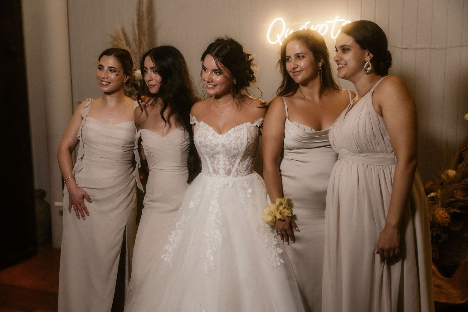 Bridesmaids in light gray dresses pose together with bride in white gown at wedding celebration.