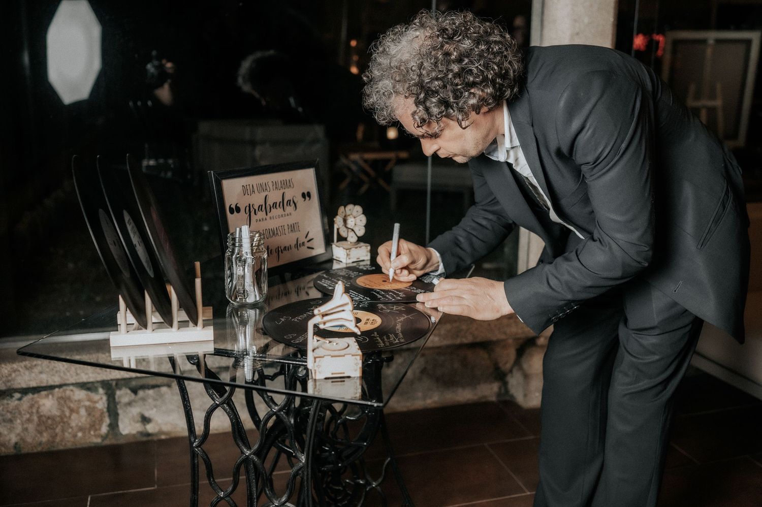 Guests sign a guestbook at an elegant wedding reception with dark moody lighting.
