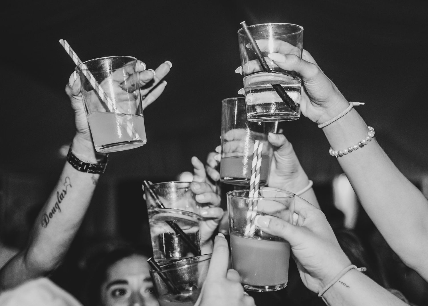 Black and white photo of raised glasses clinking together in a celebratory toast moment.