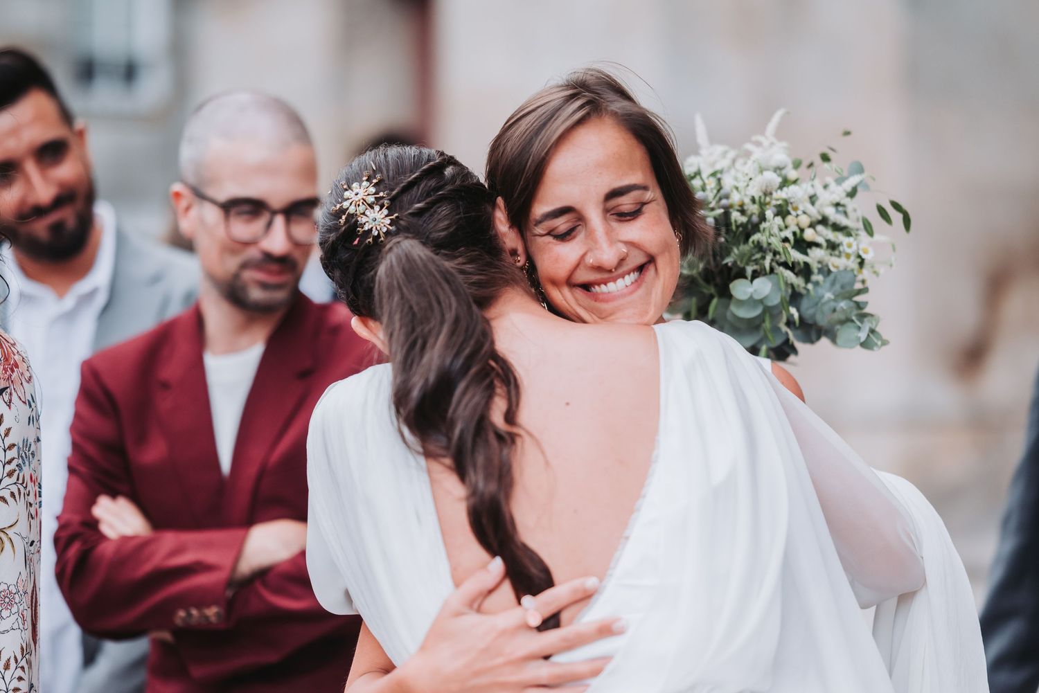 Intimate wedding celebration with guests gathered around a couple in front of a historic stone building.