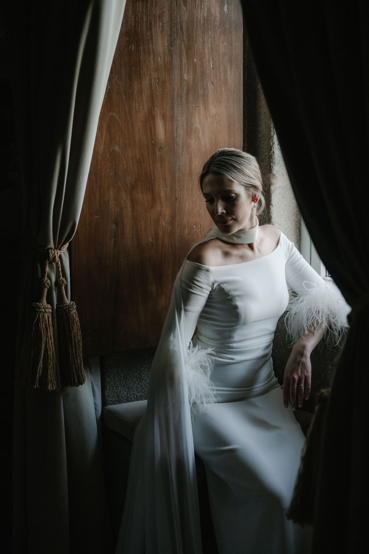 Artistic bridal portrait in white dress against dark wooden background with dramatic lighting.