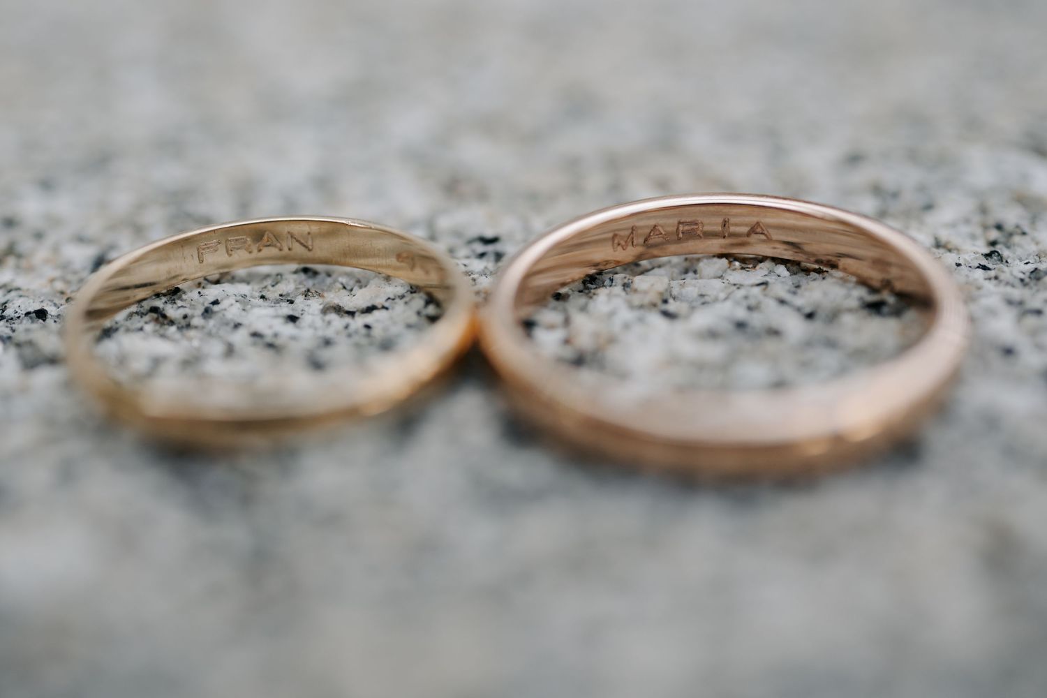 Close-up view of two gold wedding rings on a textured gray stone surface.